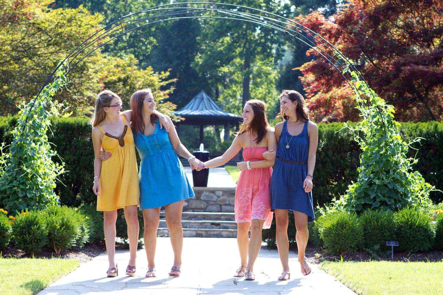 Four colorful sundresses walking together on a garden path under trees.