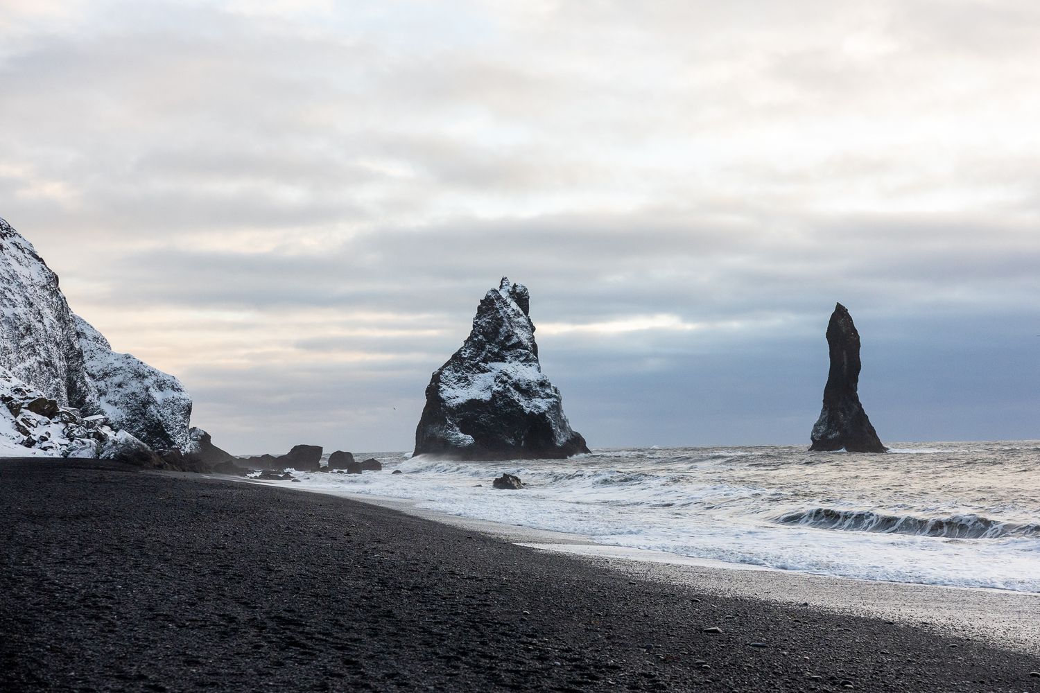 Black sand beach with dramatic rock formations and cloudy sky in Iceland.