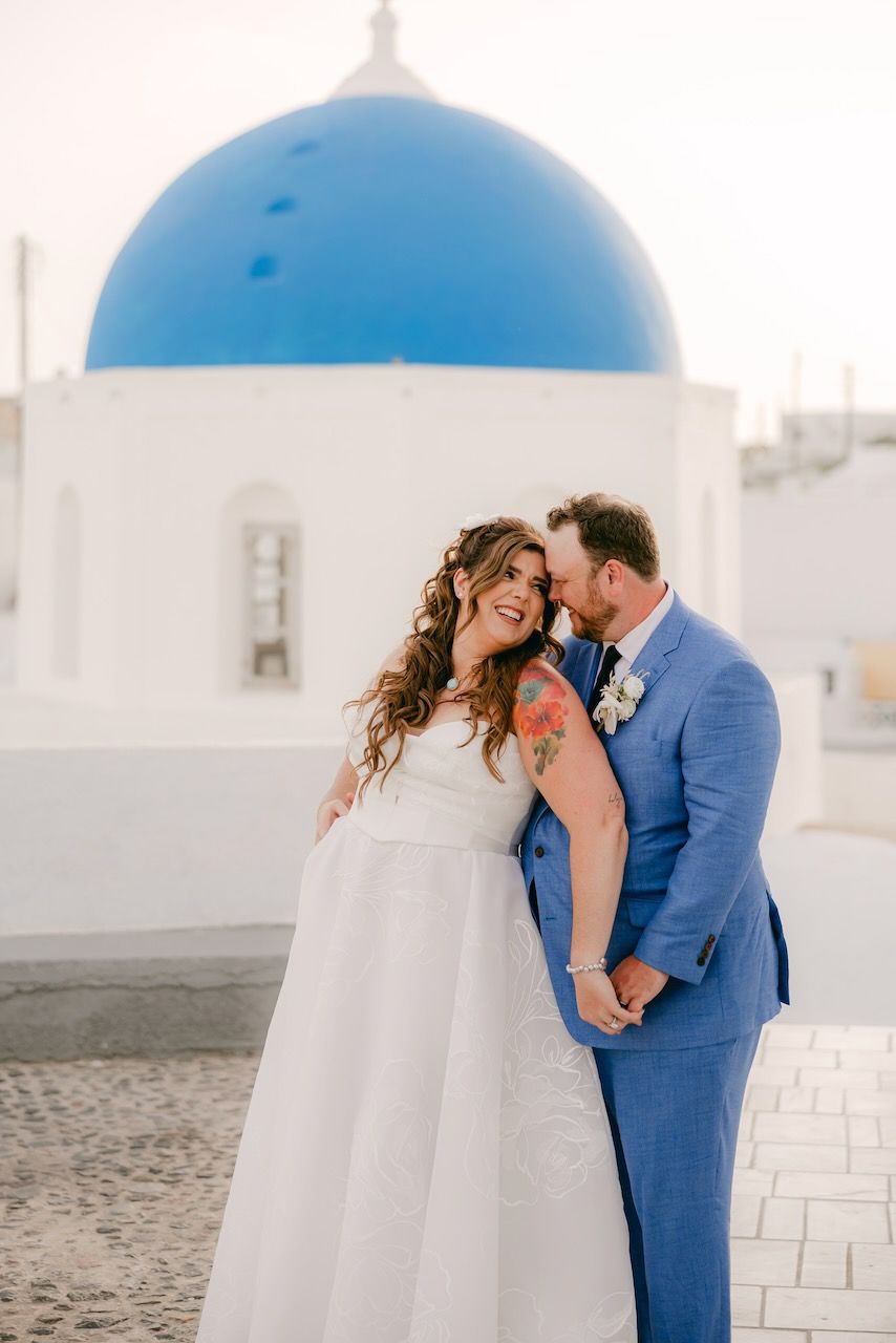 Romantic moment captured in front of white buildings with blue domes in Santorini.