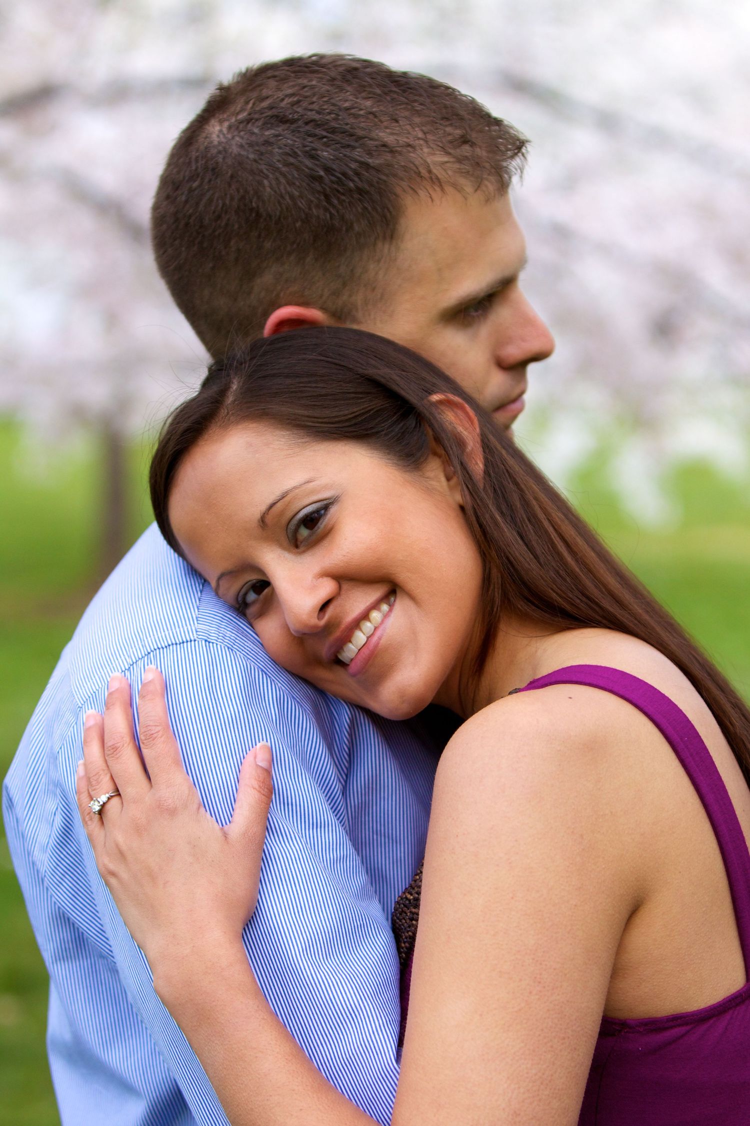 Couple sharing an intimate moment among cherry blossoms with woman in purple dress.