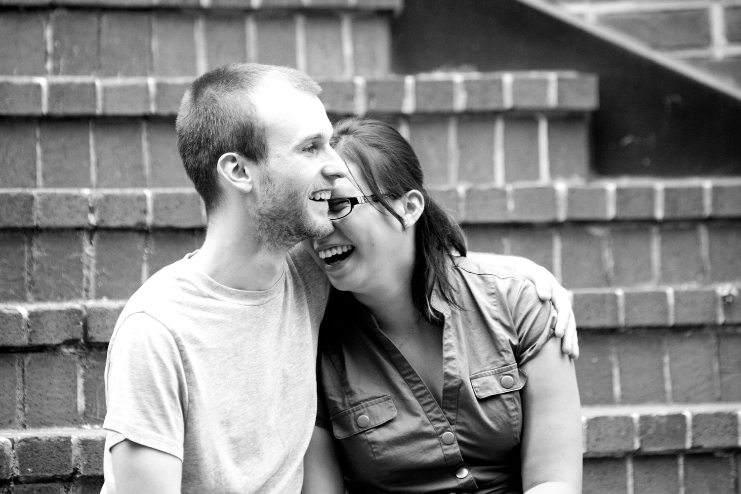 A couple shares romantic black and white moments against a brick wall backdrop.