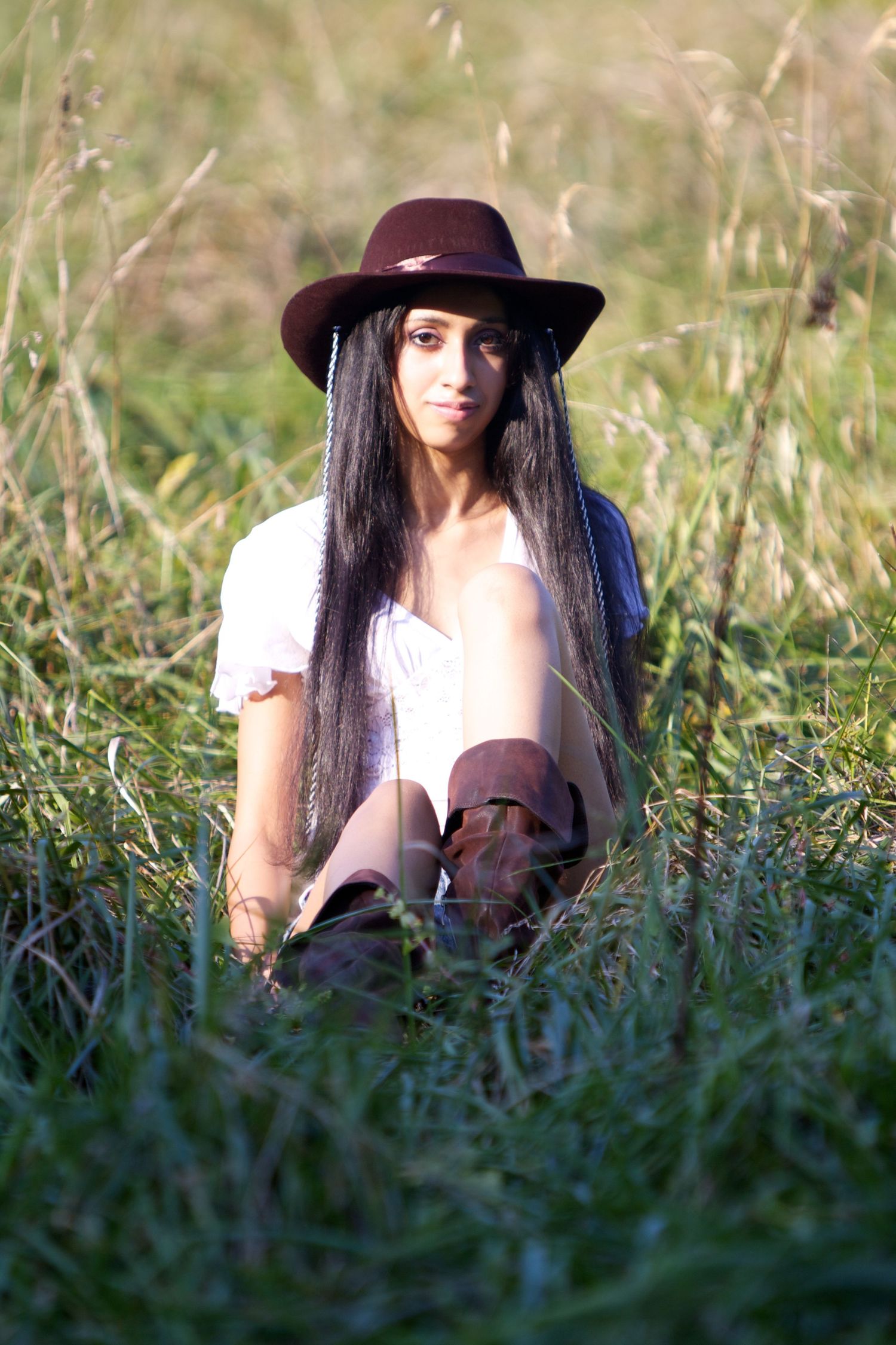 A person in a brown hat and white dress sits among tall grass in a field.