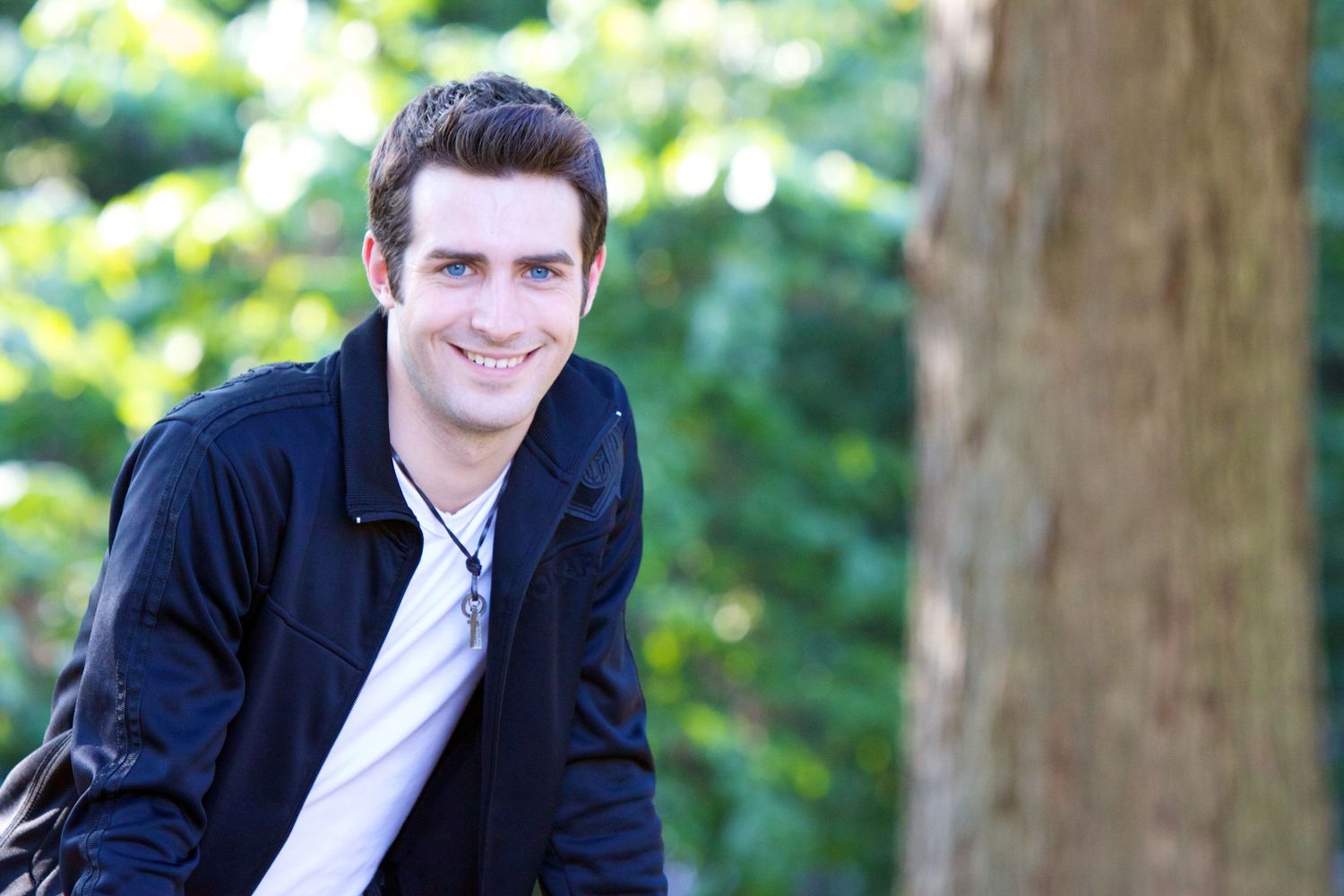 A person in a navy jacket smiles while posing outdoors against a blurred natural background.