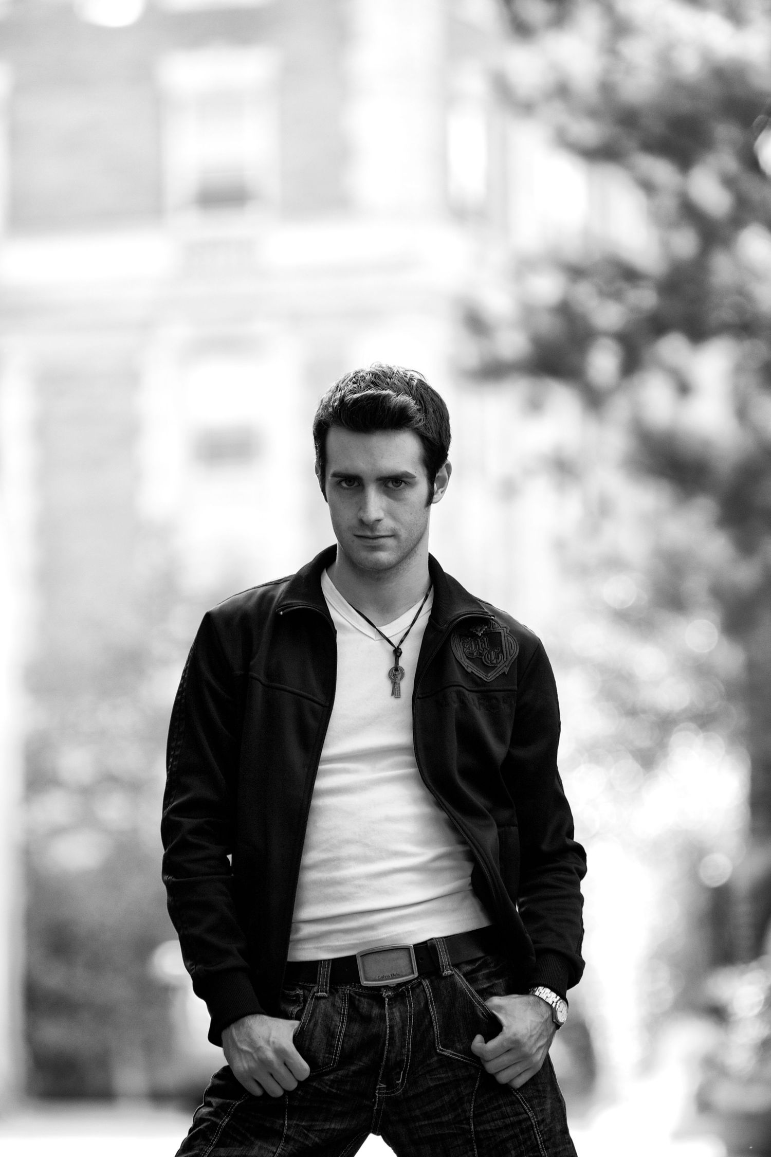 Stylish black and white portrait of someone in a leather jacket and white shirt against a blurred background.