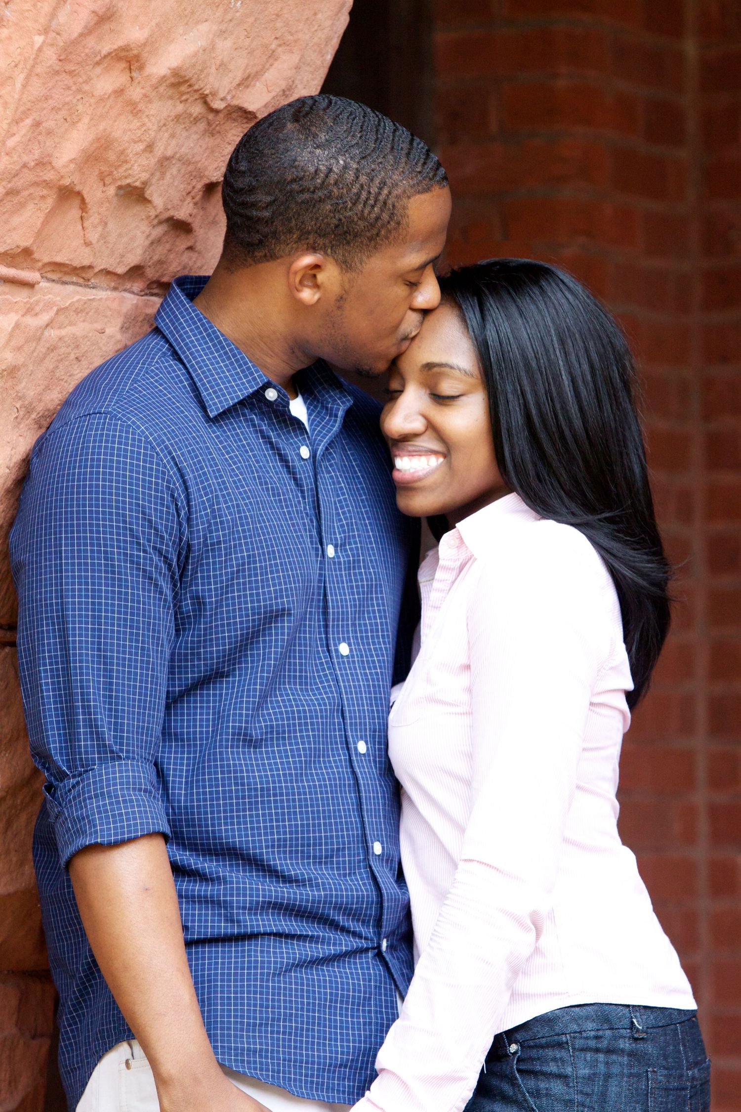 A couple shares intimate moments against a textured wall background in casual attire.