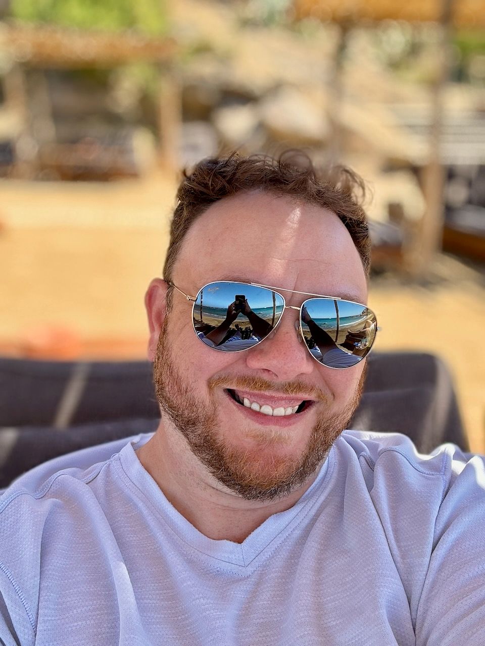 Person wearing reflective sunglasses smiling outdoors on a sunny day.