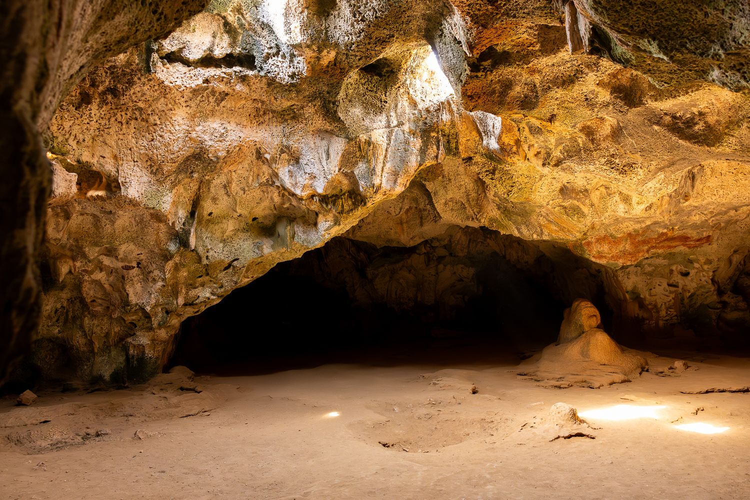 Natural cave interior with sunlight beaming through openings in the rocky ceiling.