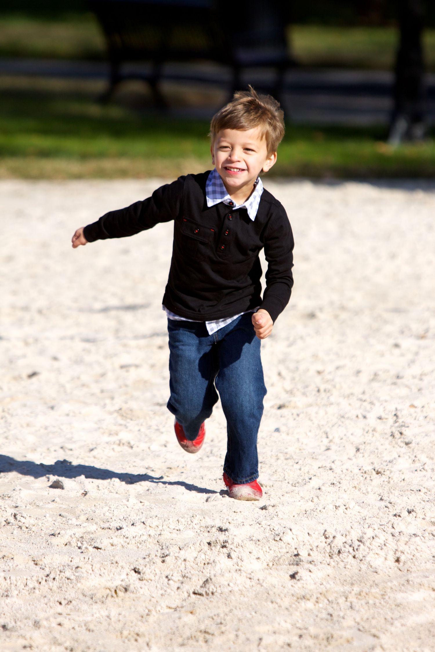 Young child running and laughing on sandy ground wearing dark sweater and jeans.