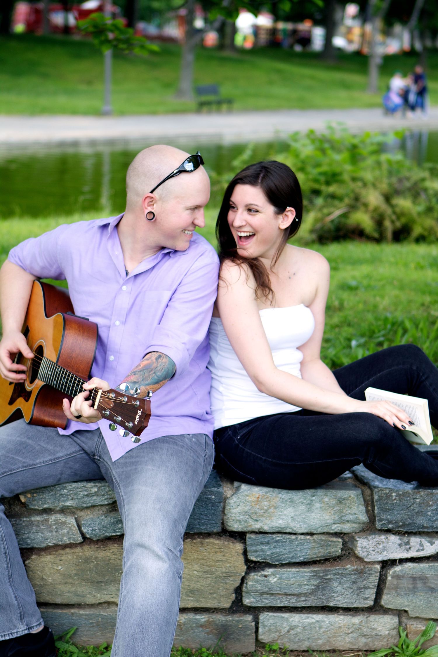 Couple enjoying music together while sitting on stone wall in park.