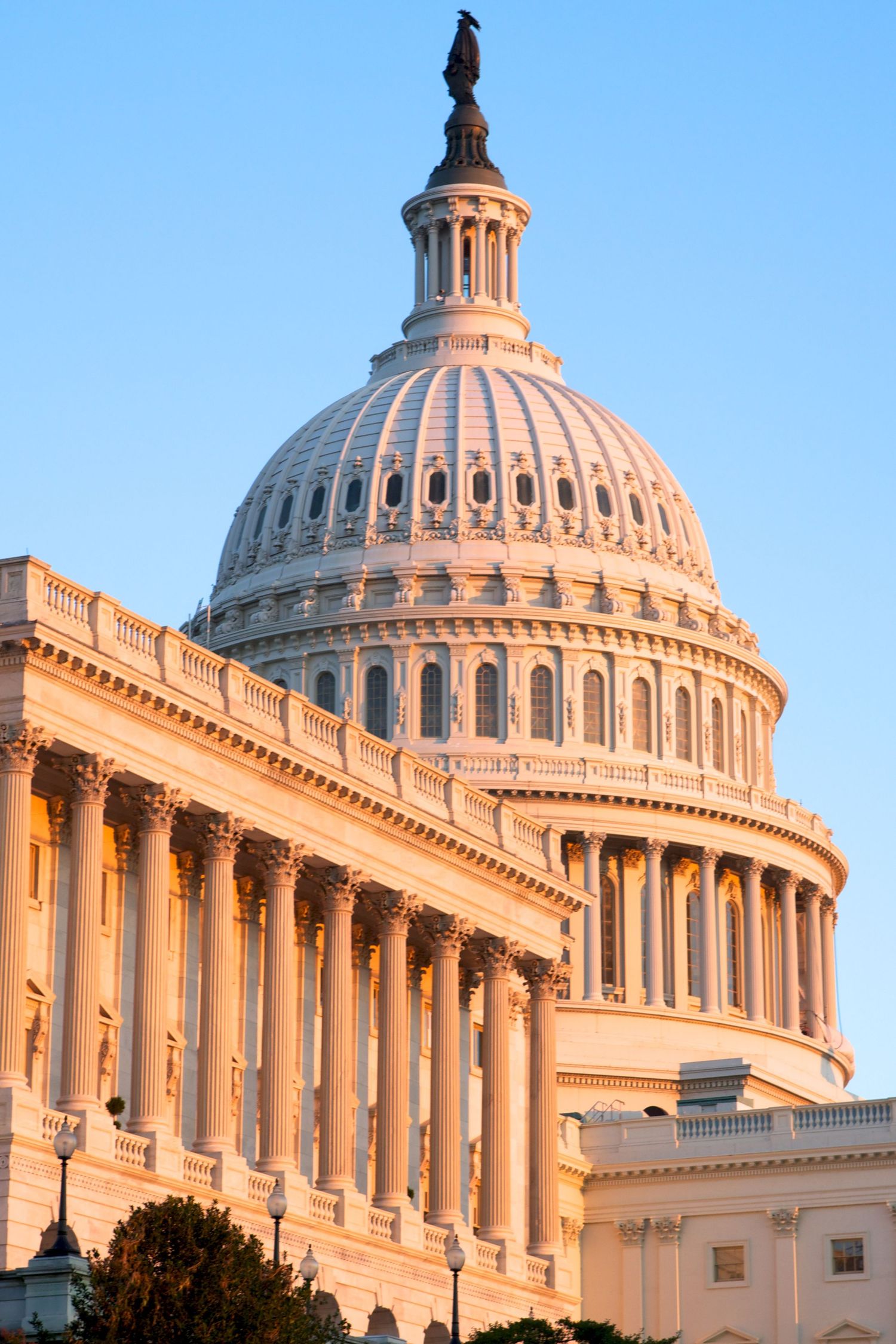 Architectural detail of the US Capitol dome and columns bathed in warm sunset light.