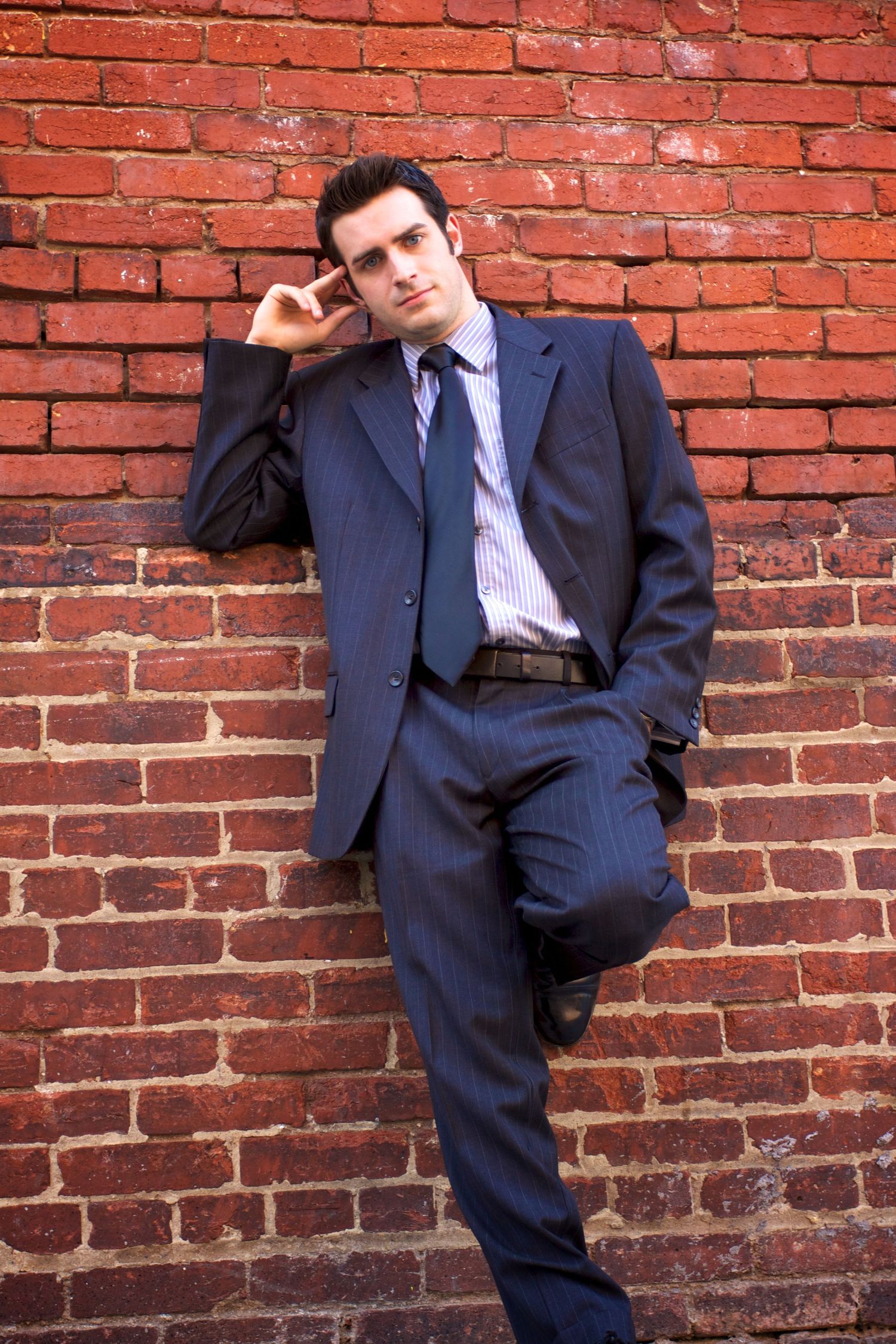 Business portraits against a red brick wall showing someone in a navy suit and dress shirt.