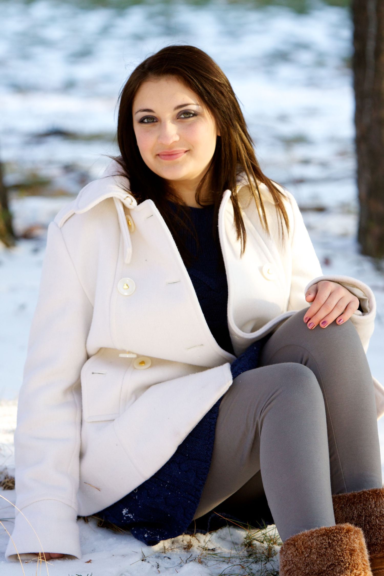 Person in white winter coat and leggings sitting on snowy ground outdoors.