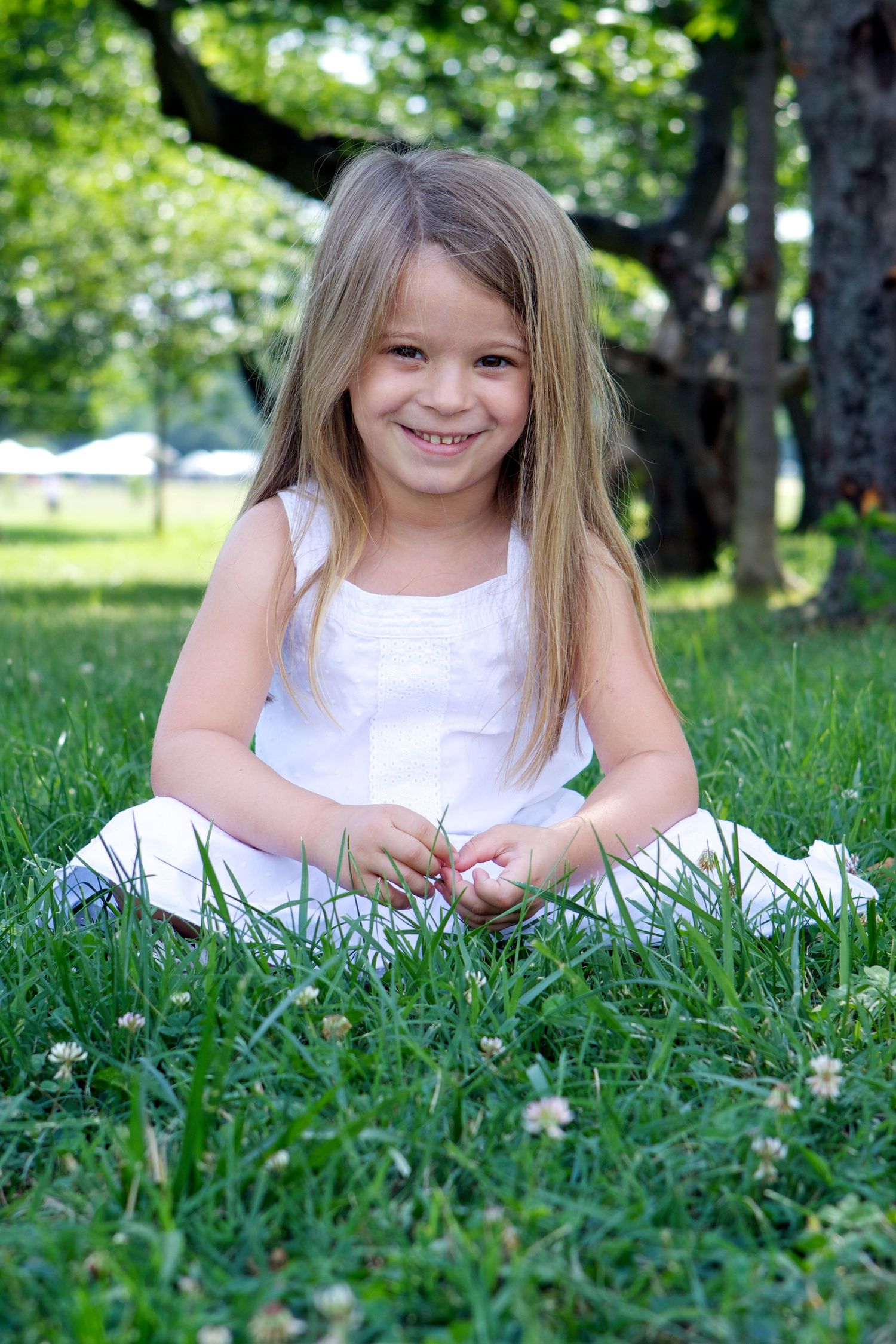 Young child in white dress sitting in green grass on summer day.