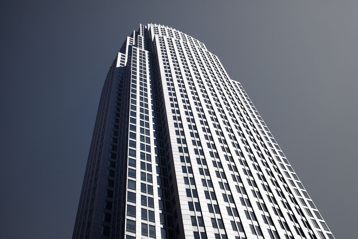 Low angle view of a modern skyscraper with geometric windows against grey sky.