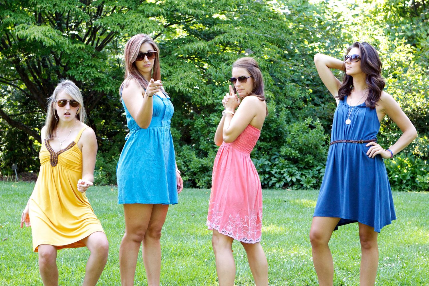 Four colorful summer dresses in yellow, blue, pink and navy displayed in a garden setting.
