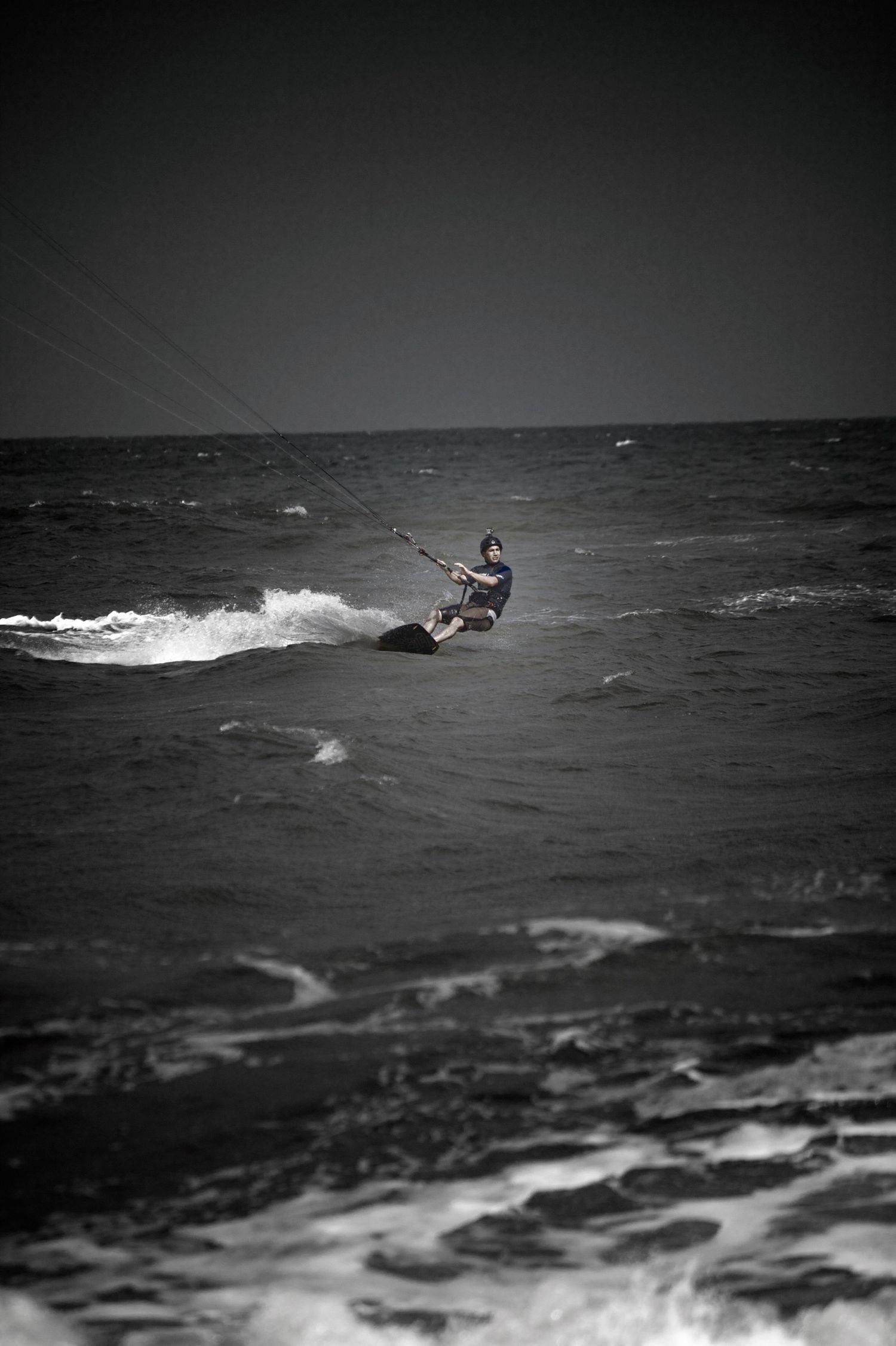 Black and white photo of kitesurfing action on rough ocean waves.