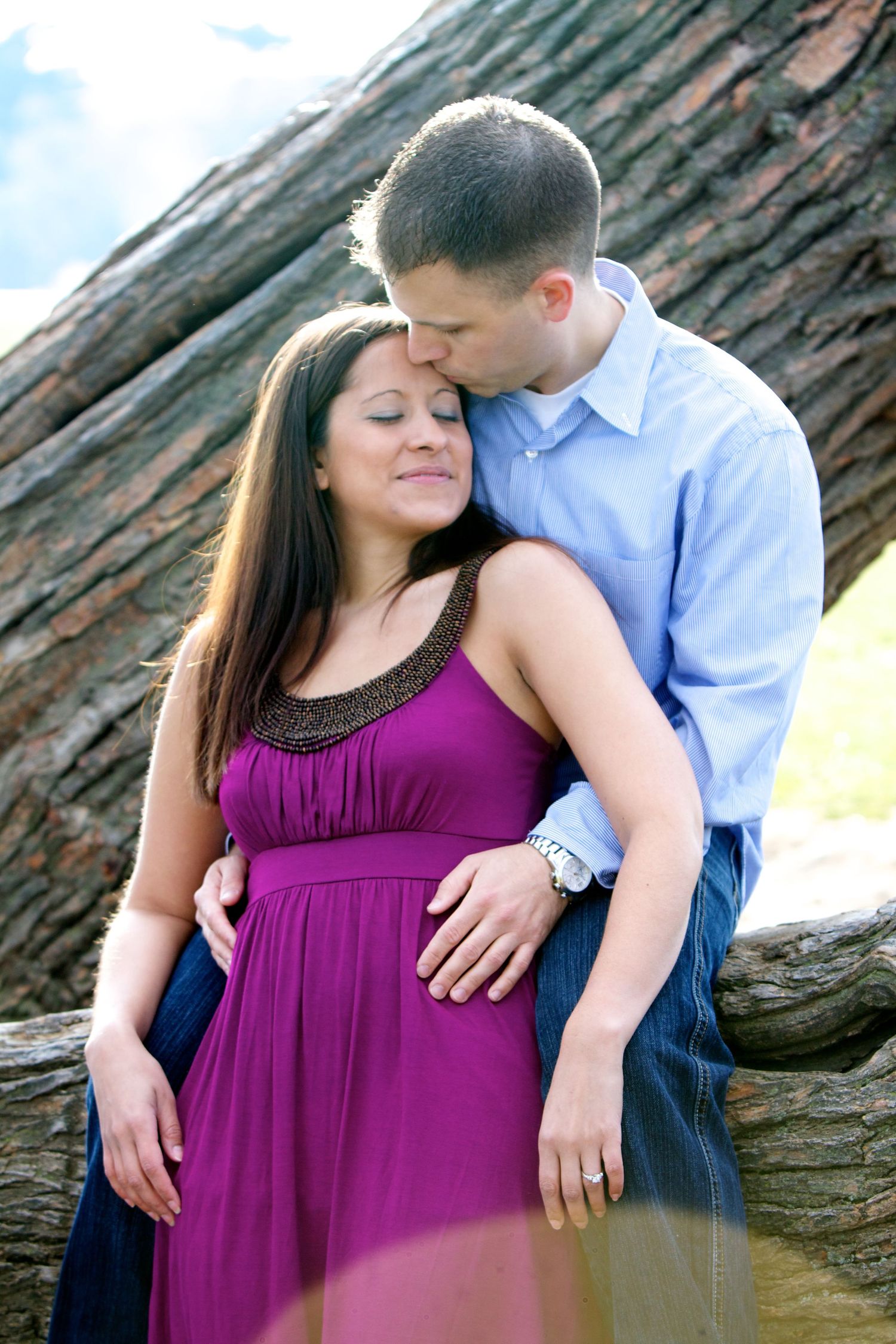 Romantic couple embracing by a large tree trunk during an outdoor photo session.