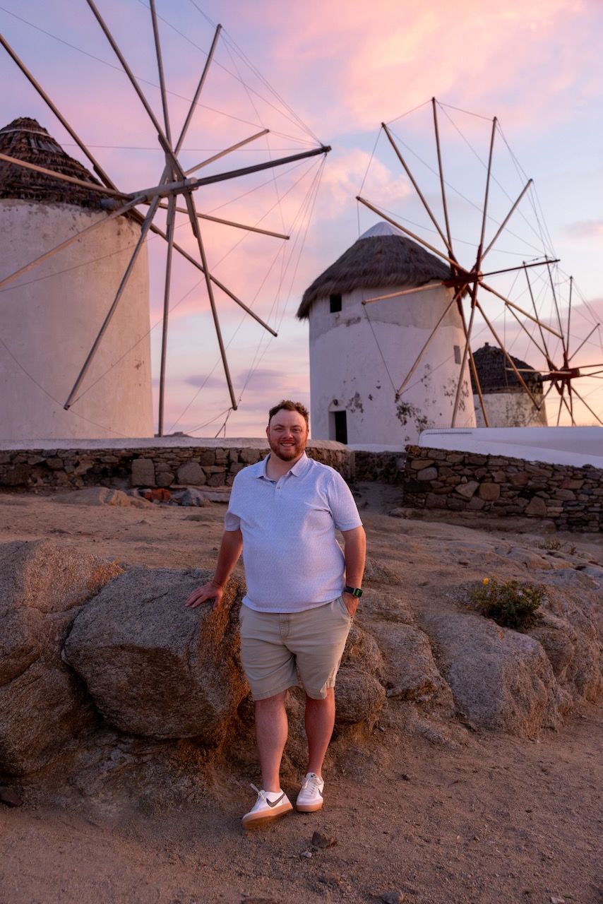 Traditional white windmills against a pink sunset sky in a Mediterranean setting.