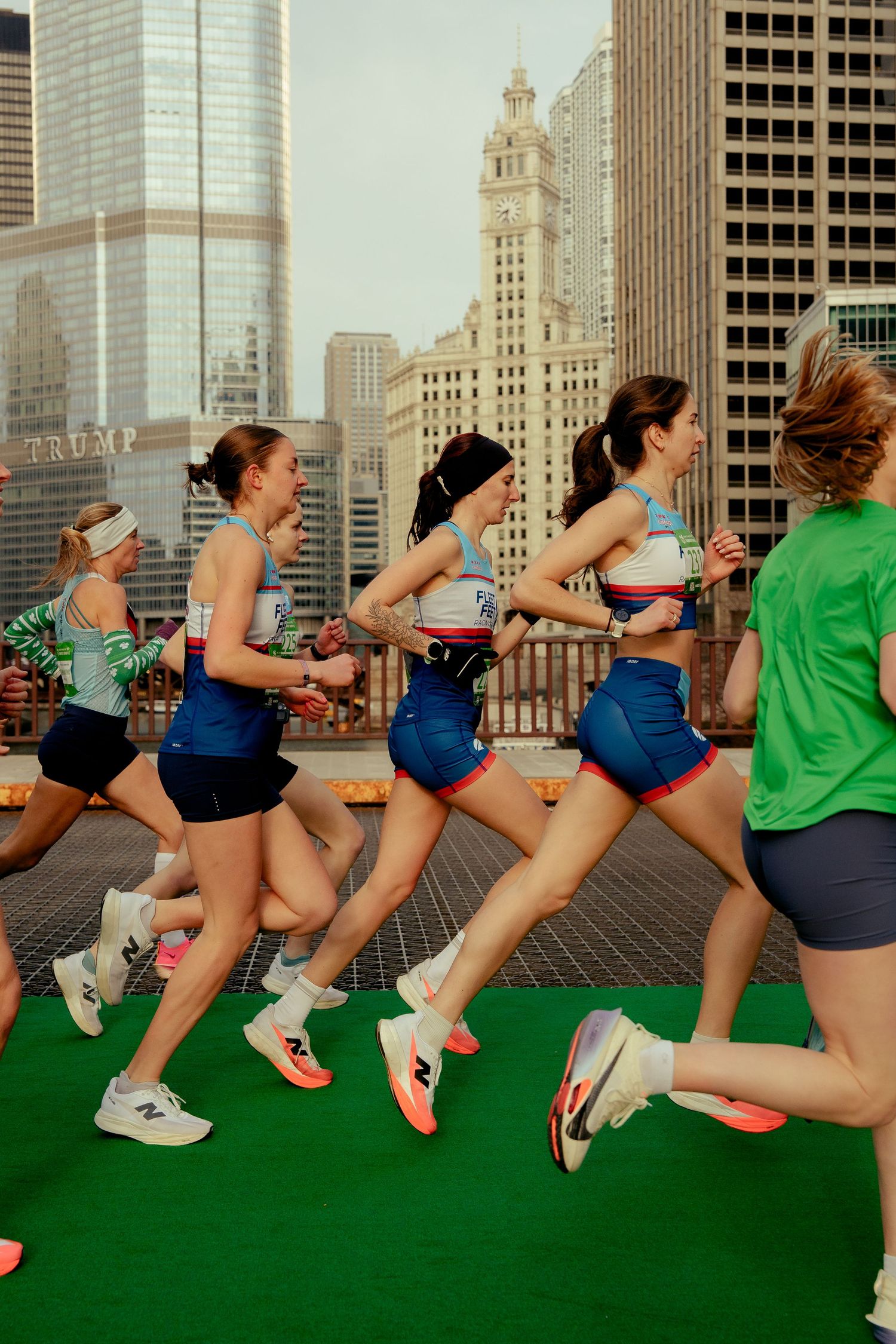 Female runners race through Chicago's skyline, wearing colorful athletic gear, with Trump Tower visible in the background.