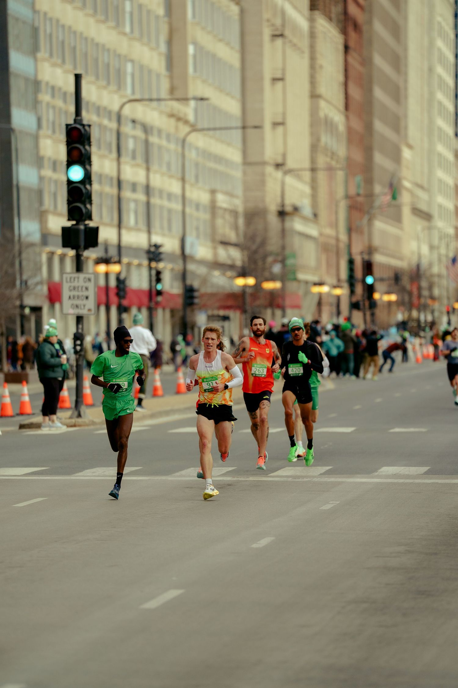 Runners compete in a street marathon through downtown Chicago, passing traffic lights and urban buildings.