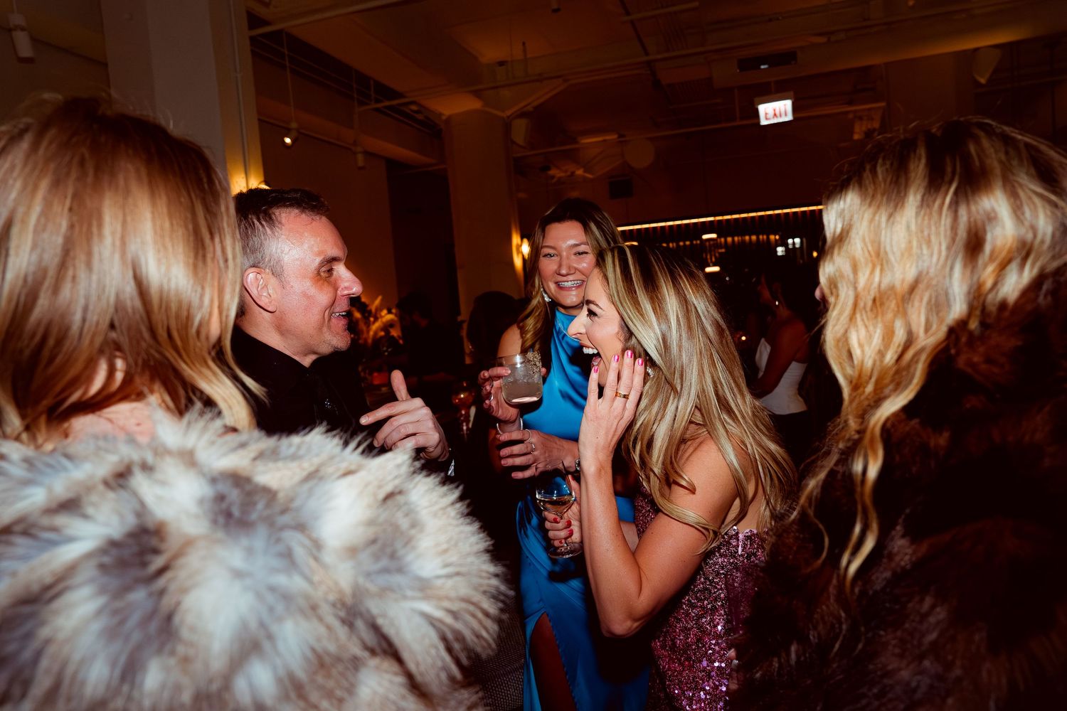 Lively party scene with guests laughing and socializing in a warmly lit room.