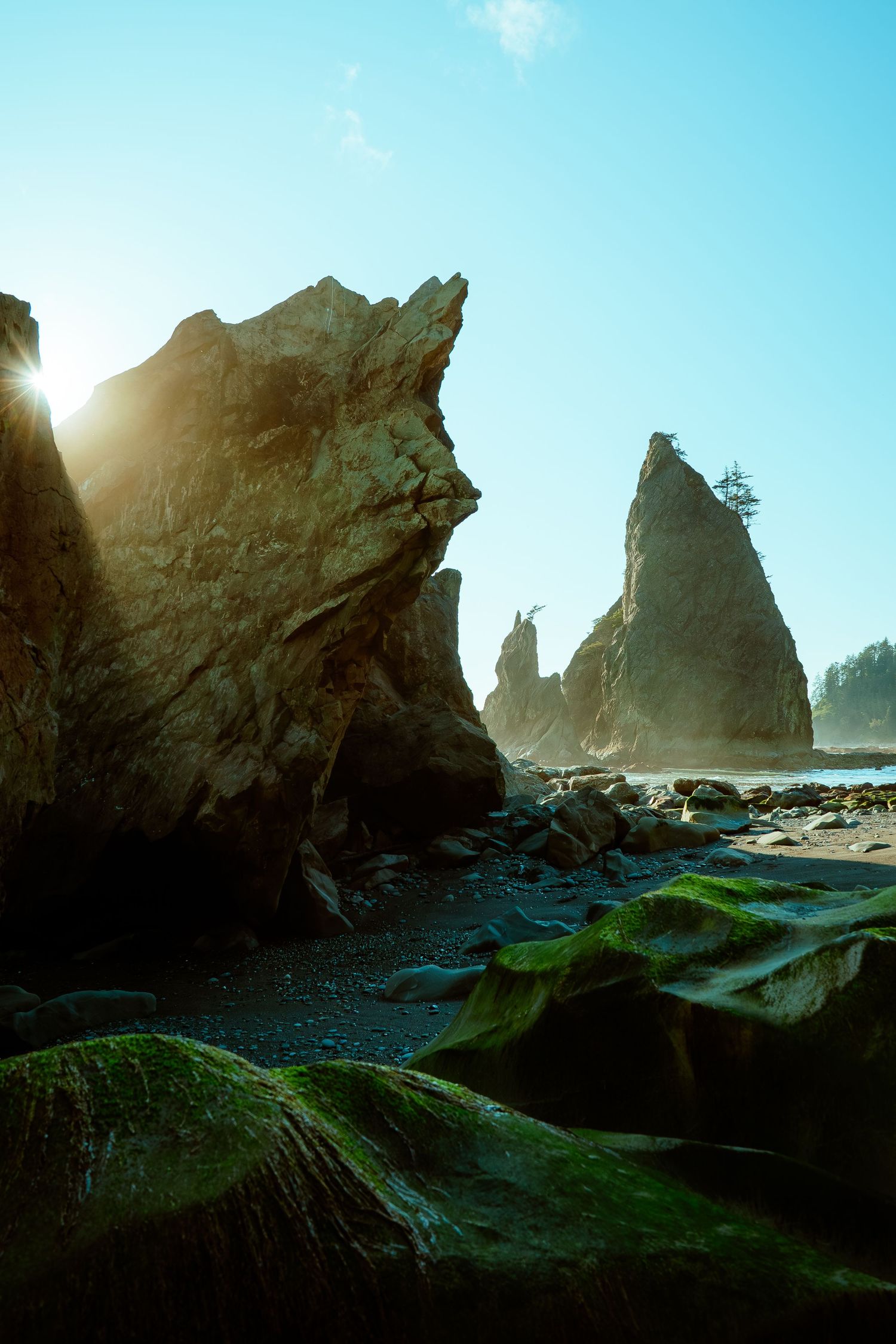 Dramatic rocky sea stacks and cliffs along a coastal beach at sunset.