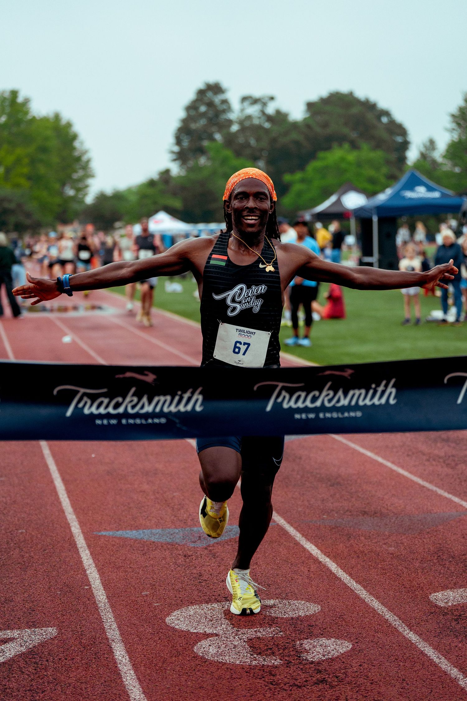 Track athlete crossing finish line with arms outstretched at outdoor competition.