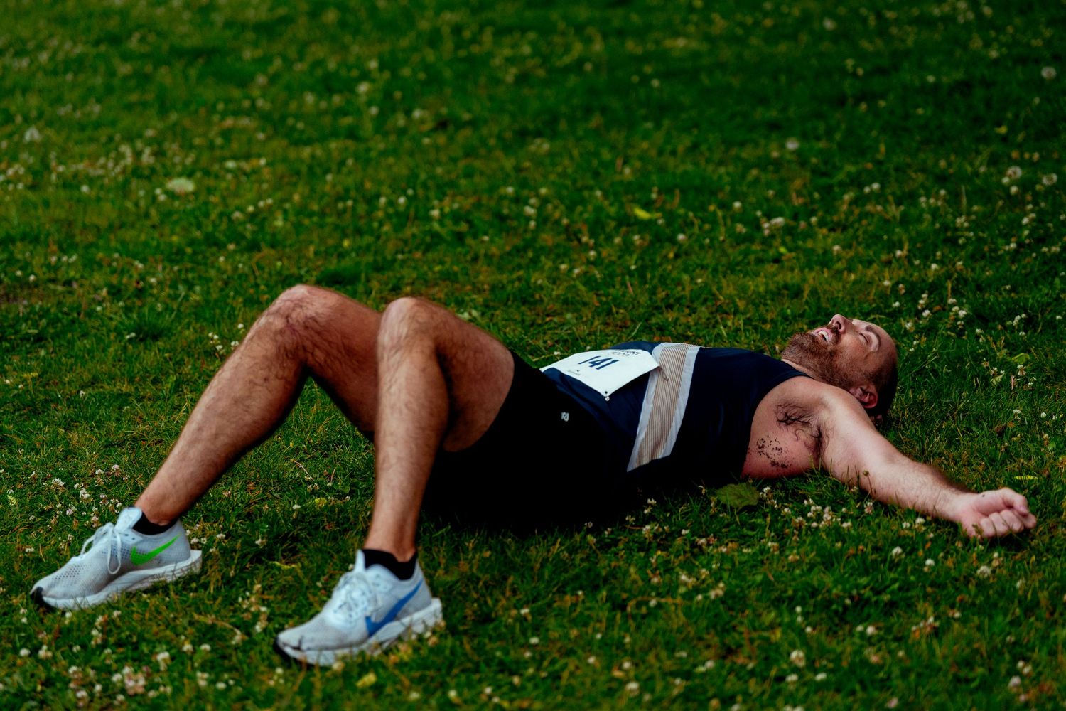 Athletes lying exhausted on grass field after competition.