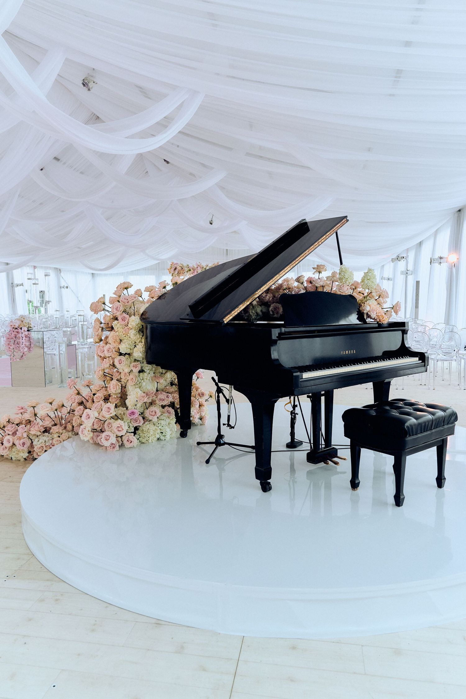 Three grand pianos arranged on white circular platform with floral decorations in elegant event space.