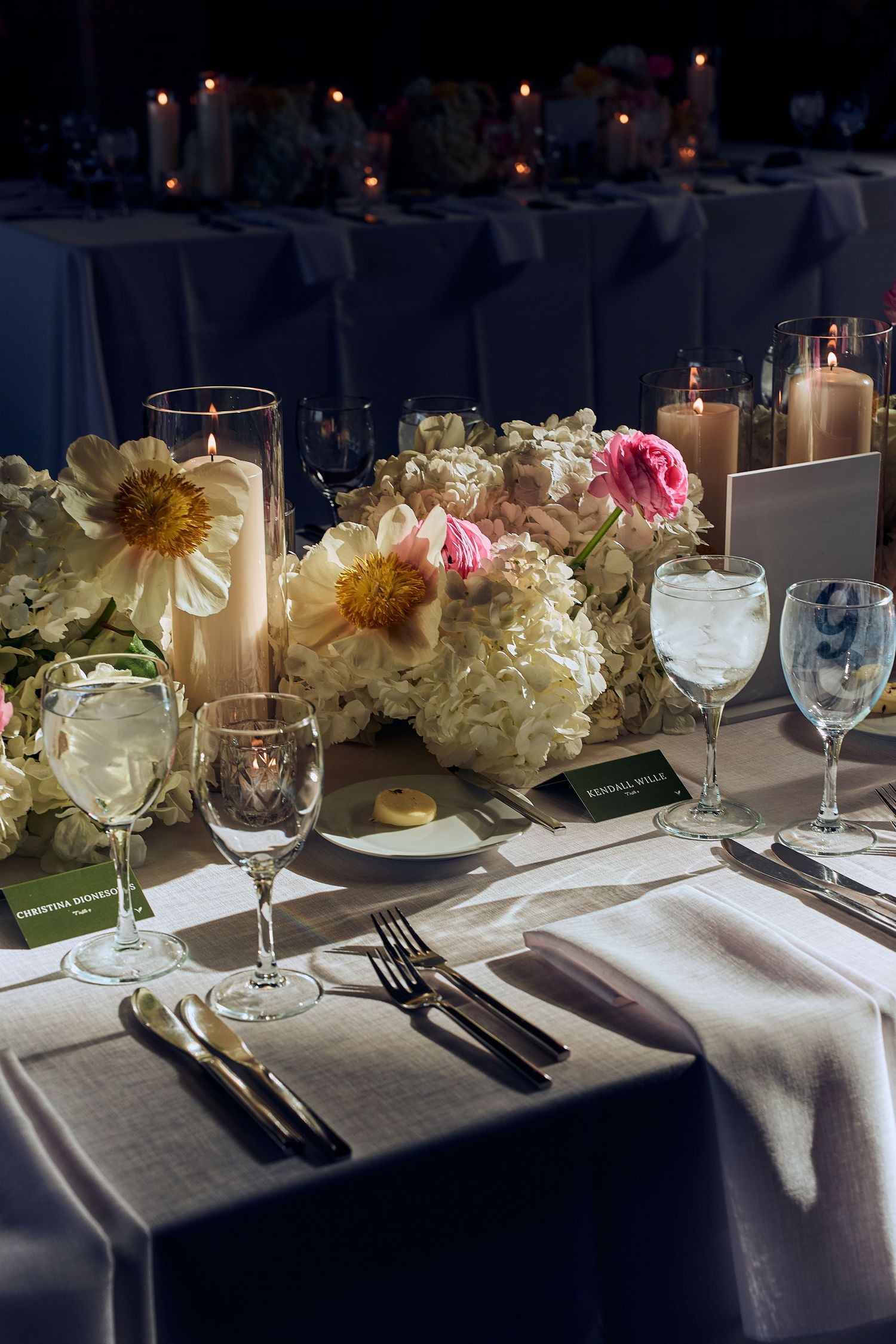 Elegant table setting with white floral centerpieces, wine glasses, and place settings at a formal dinner.