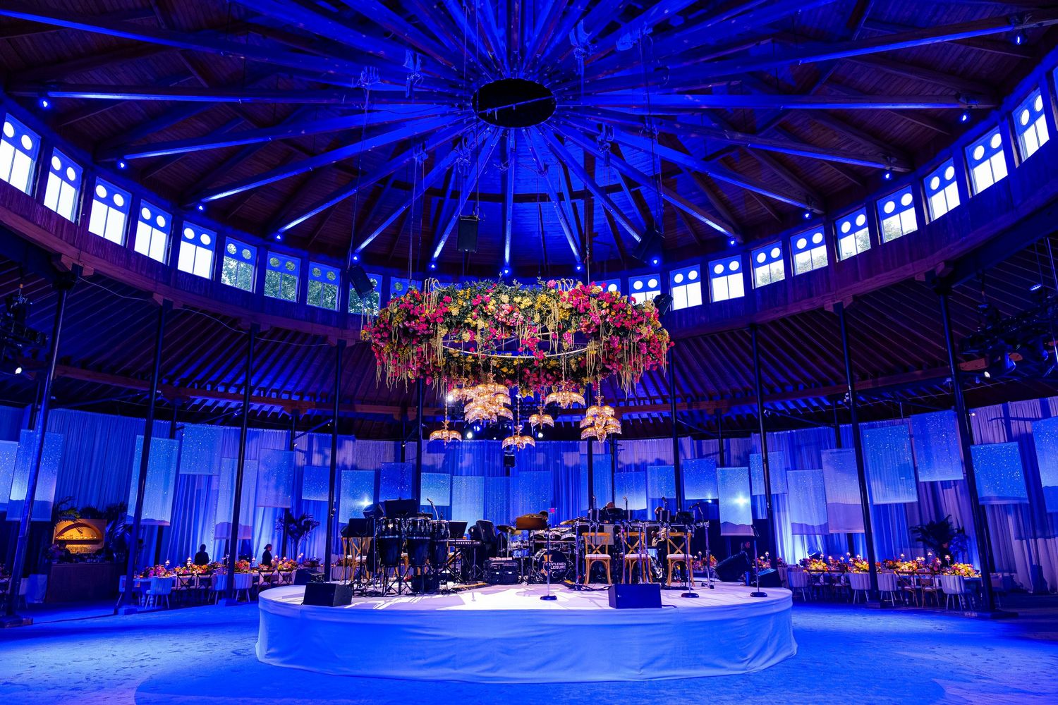 Concert stage setup with dramatic blue lighting and floral chandelier in a circular venue.