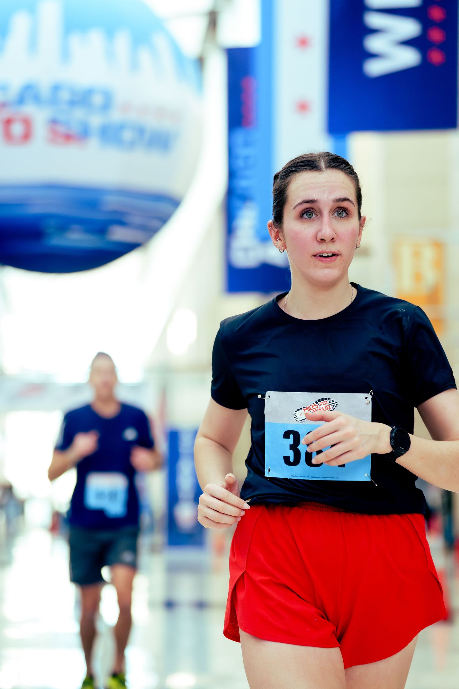 Runner wearing black shirt and red shorts participates in indoor race event.
