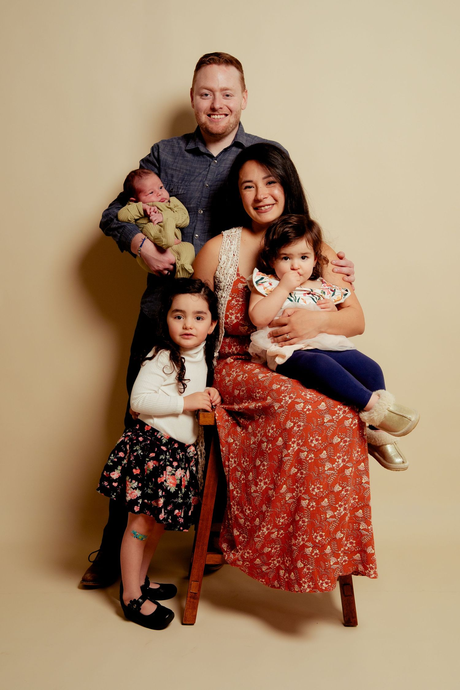 Family portrait of parents with three young children, including a newborn, posing together in a professional studio setting.