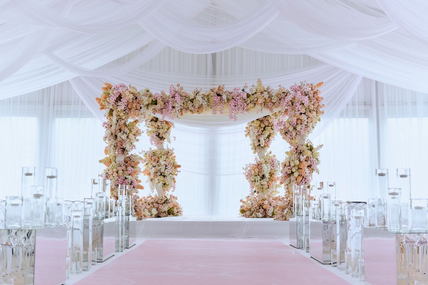 Luxurious white wedding venue with draped ceiling and pink floral arrangements.