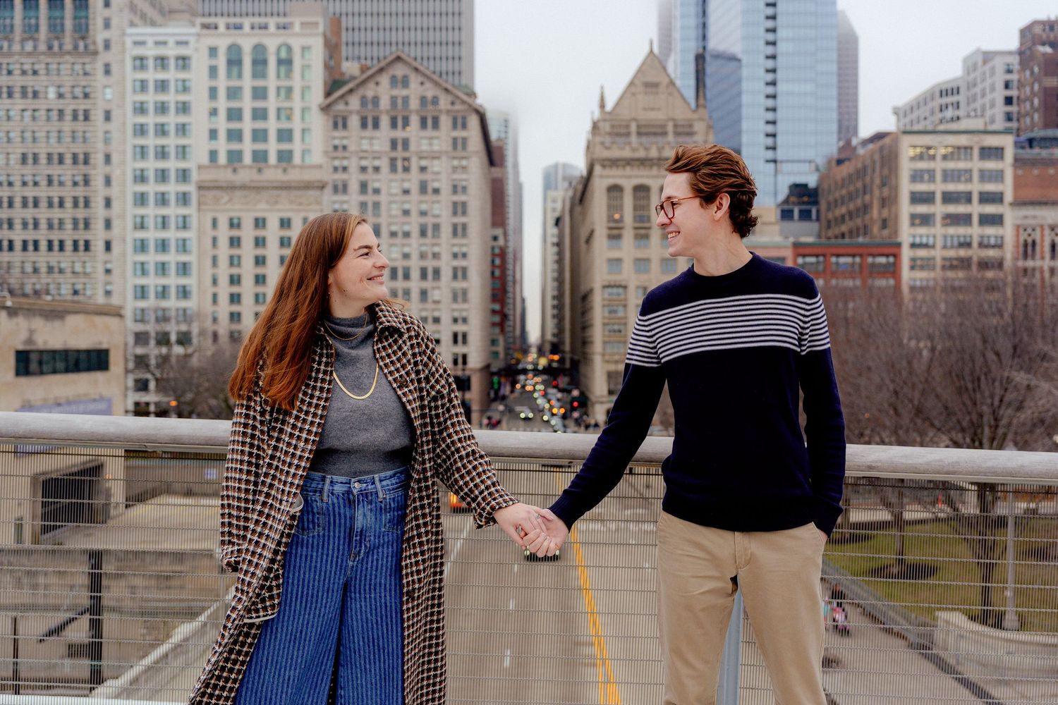 A couple shares a romantic moment on a city bridge with urban buildings in the background.