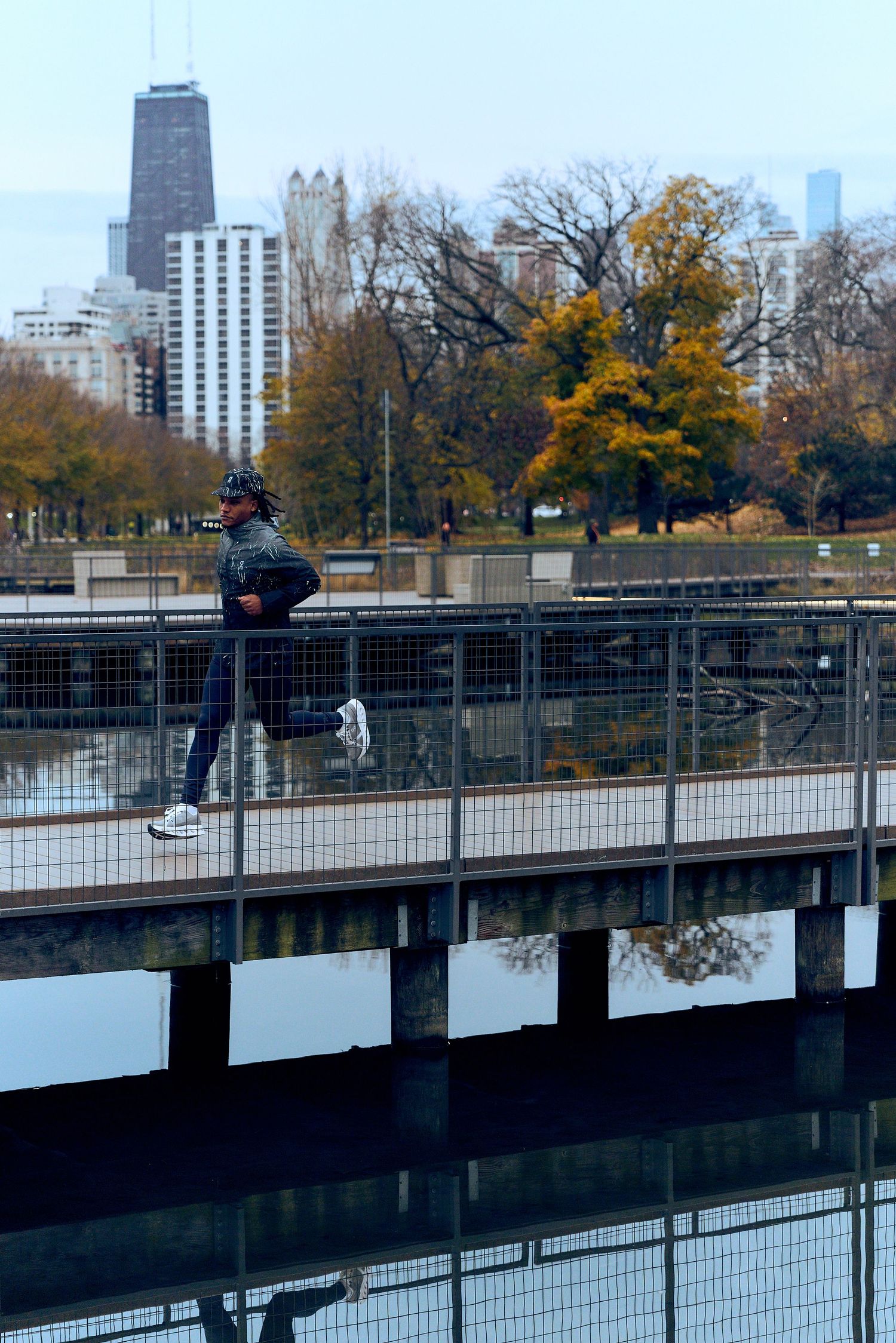 Person standing on a bridge overlooking a city skyline with autumn trees in an urban park setting.