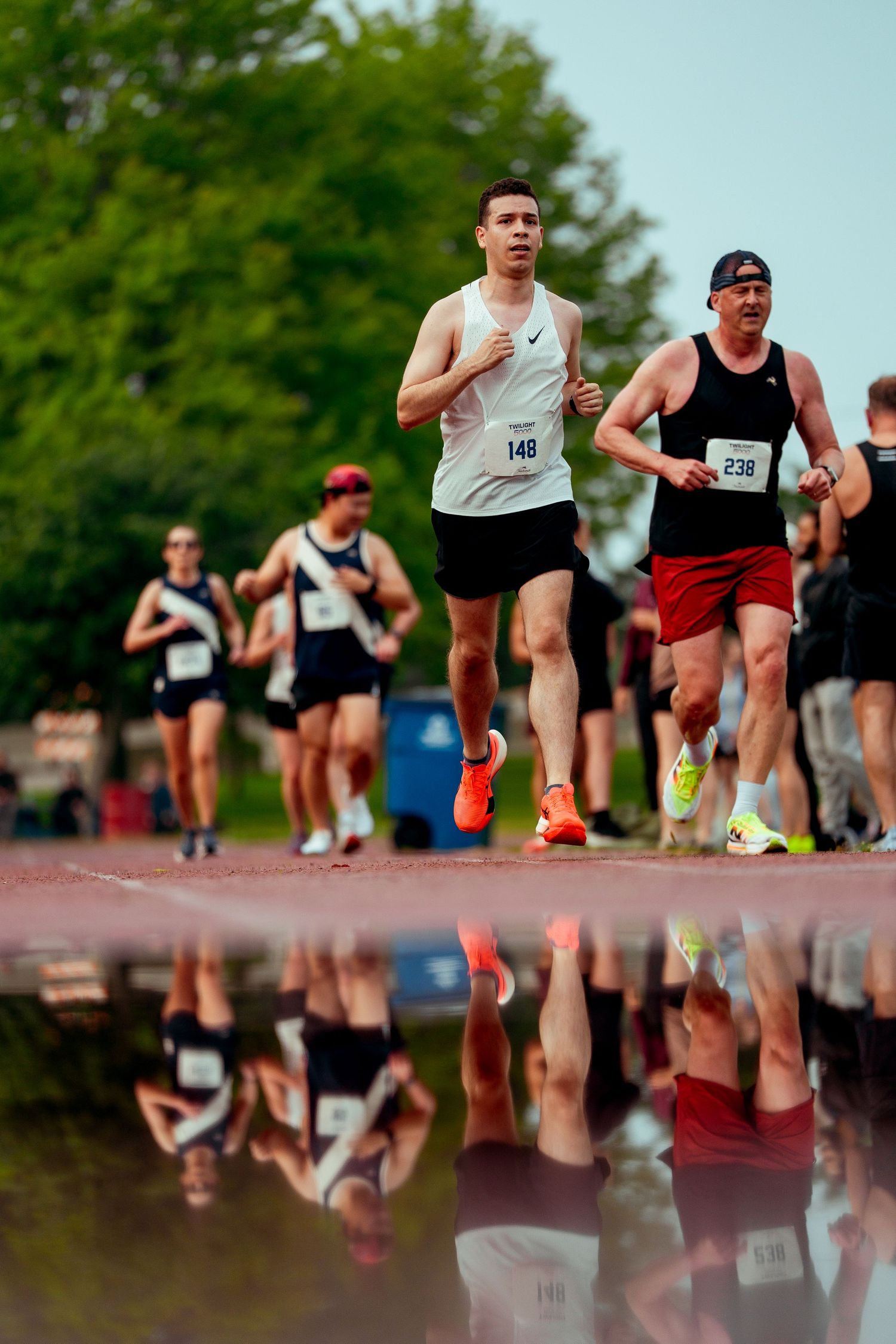 Runners reflected in puddle during outdoor track meet competition.