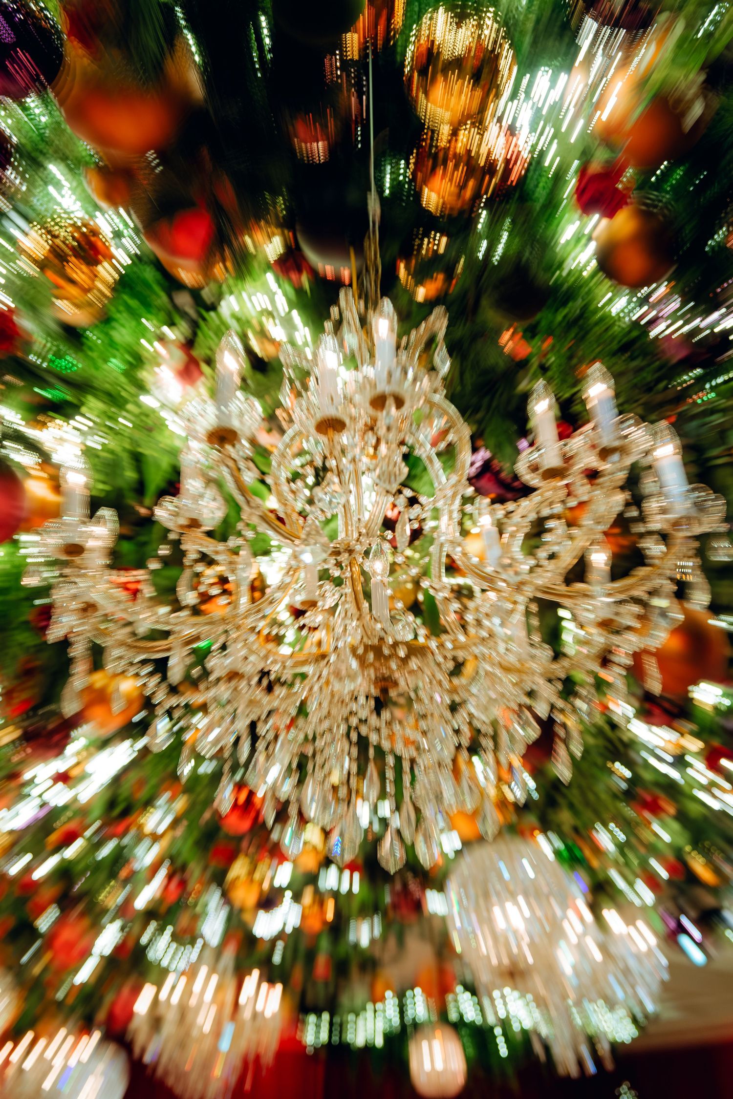 Abstract zoom effect photo of a crystal chandelier with holiday decorations creating a starburst pattern.