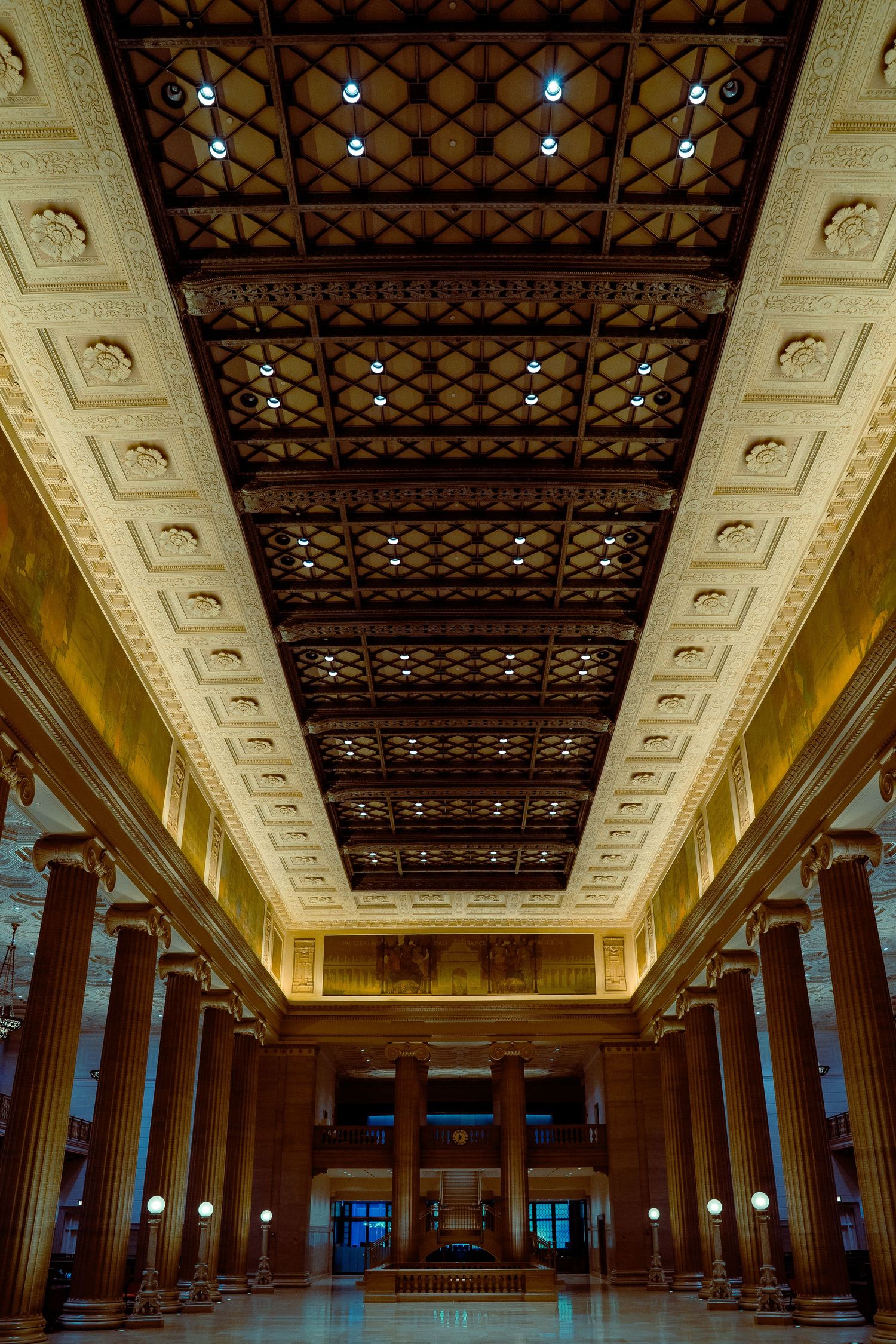 Ornate historic hall interior with decorative ceiling, columns and warm lighting.