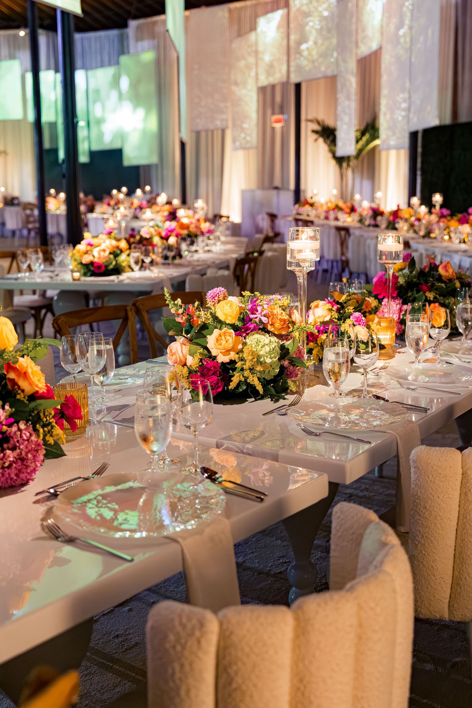Elegant wedding reception tables with colorful floral centerpieces and crystal glassware in a modern venue.