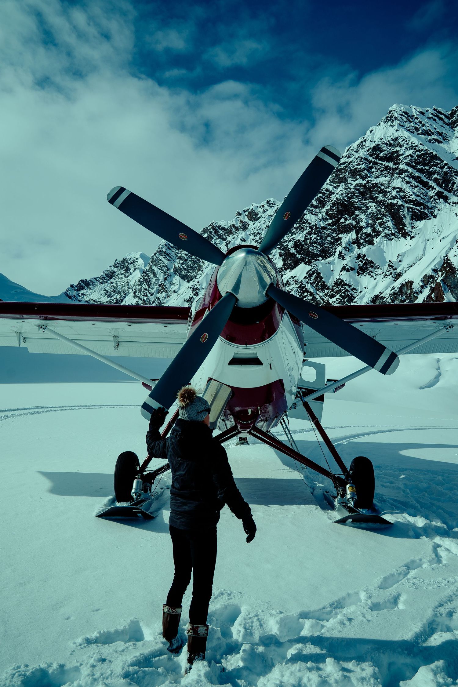 Small propeller plane on snowy terrain with snow-capped mountains in background.