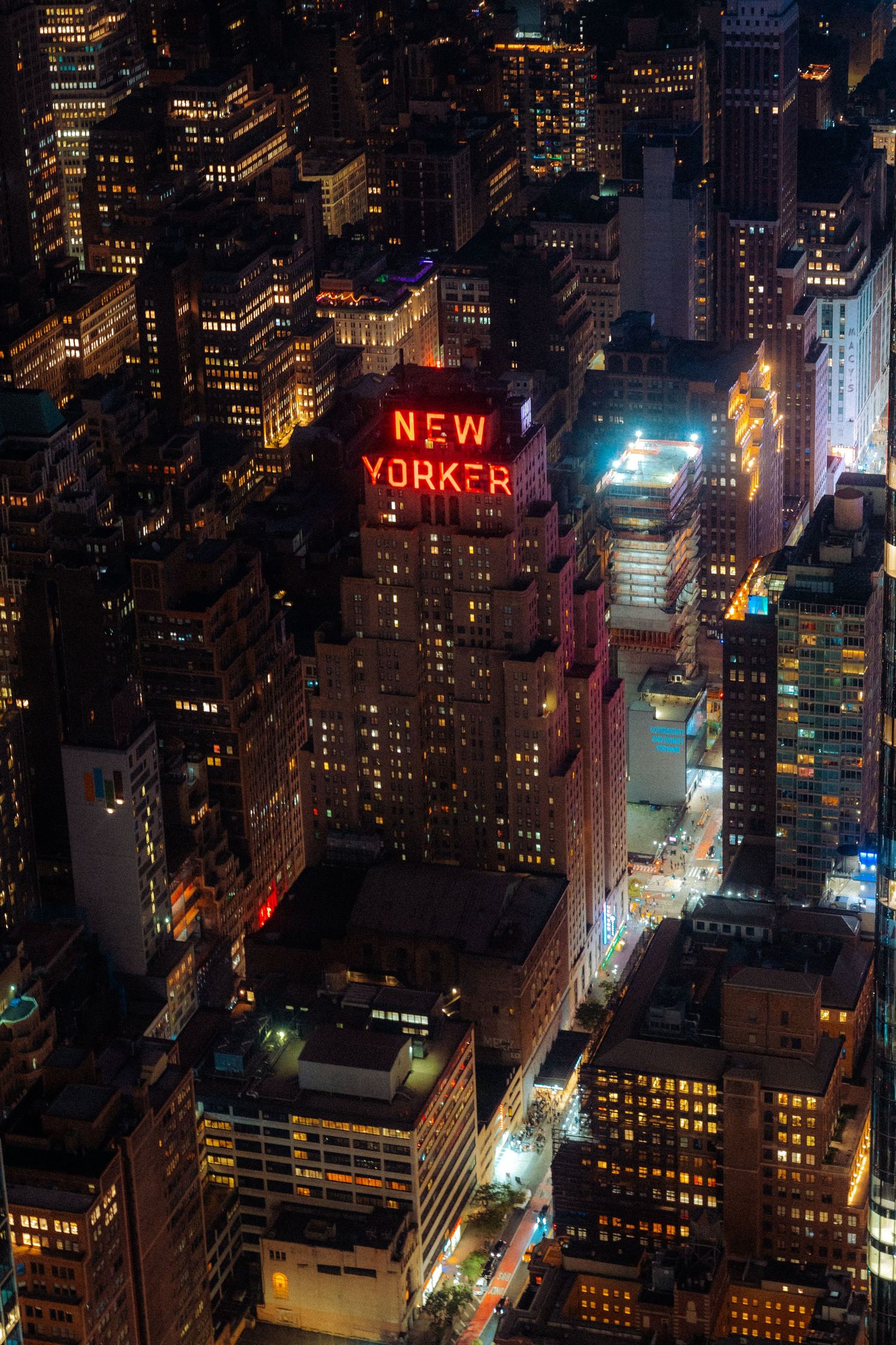 Aerial view of New York City at night with illuminated buildings and iconic New Yorker sign.