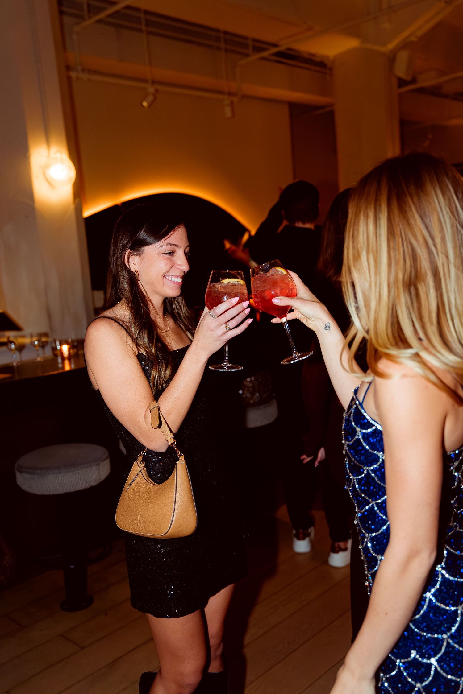 Party guests toasting with wine glasses at a dimly lit celebration event.