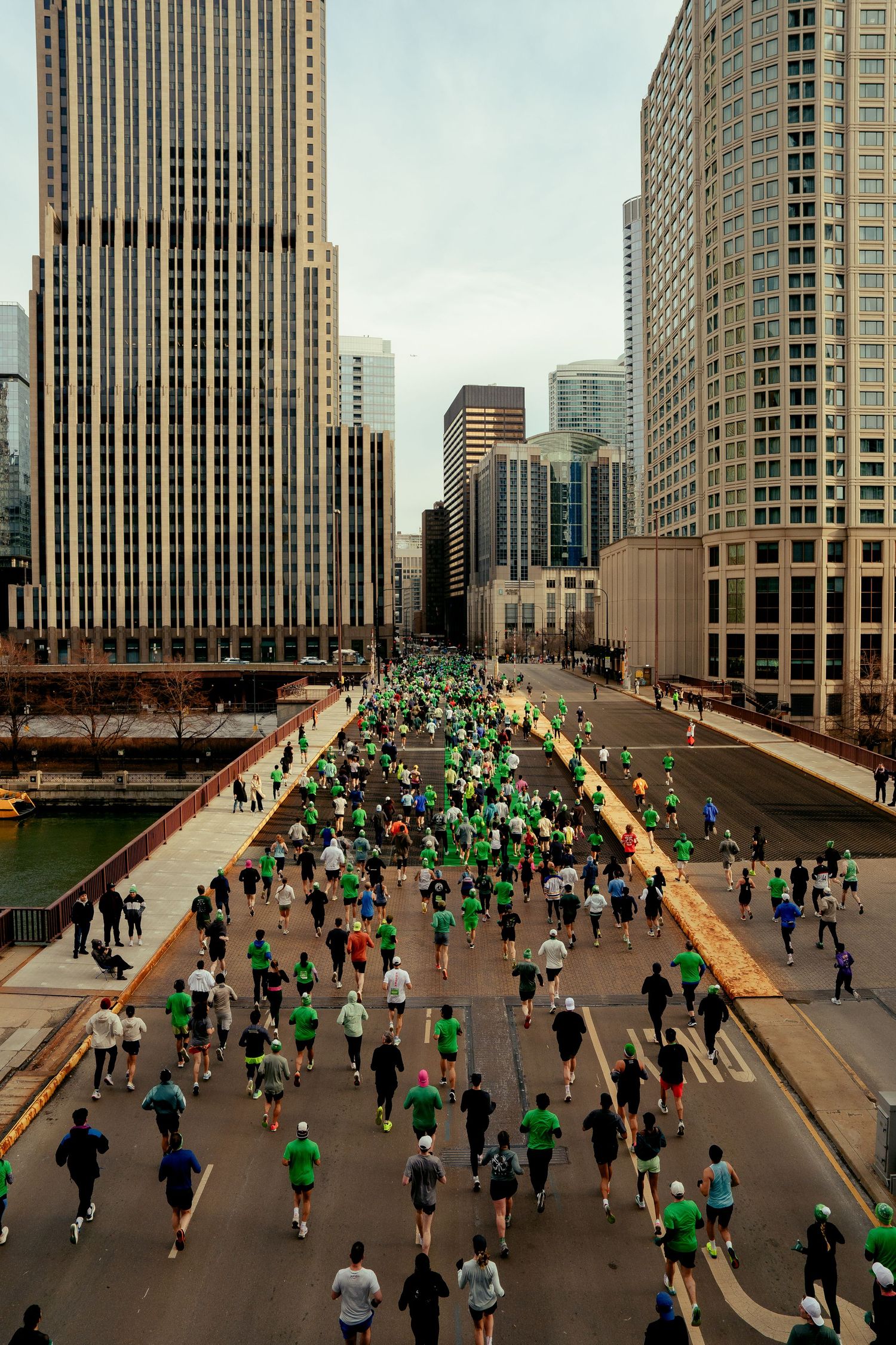 Aerial view of runners in green attire racing through downtown Chicago streets during a St. Patrick's Day marathon.