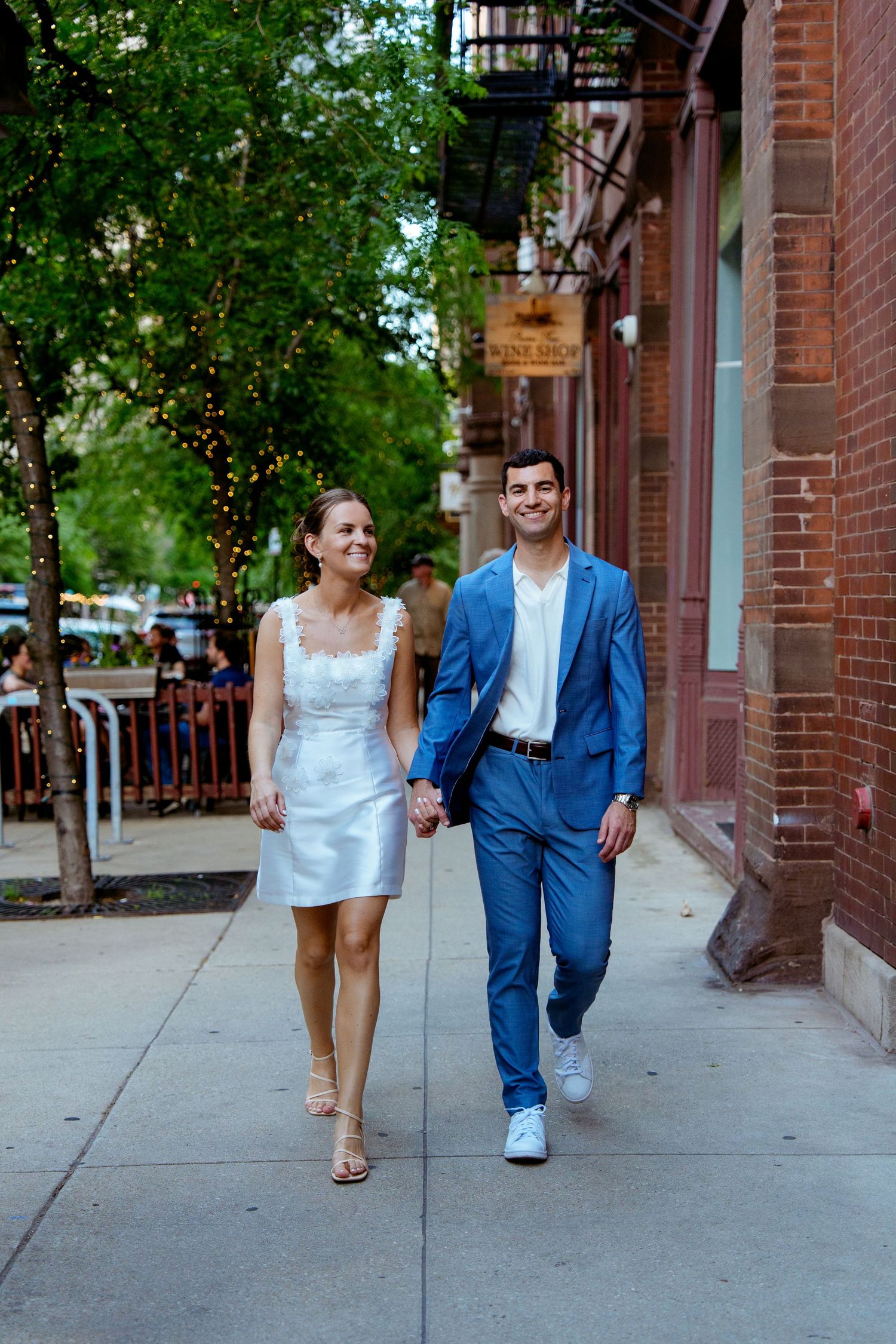 Couple walking along a brick sidewalk in formal attire.