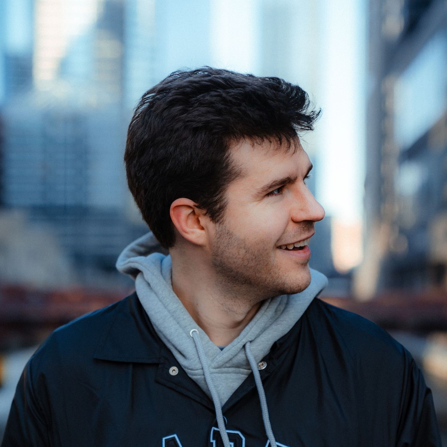 Person in casual winter attire looking to the side against an urban backdrop.
