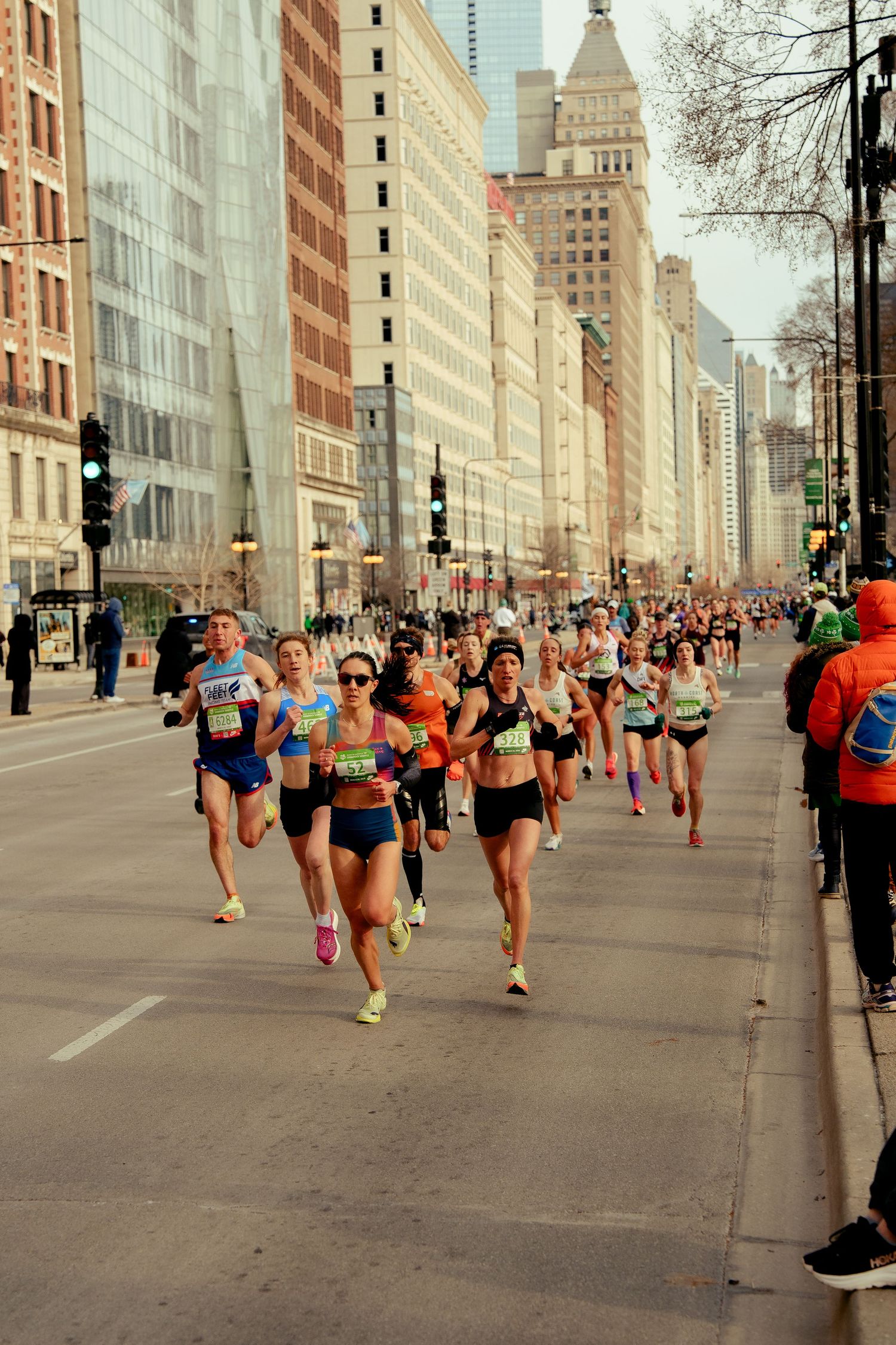 Runners compete in a city marathon race along a wide urban street lined with tall buildings in Chicago.