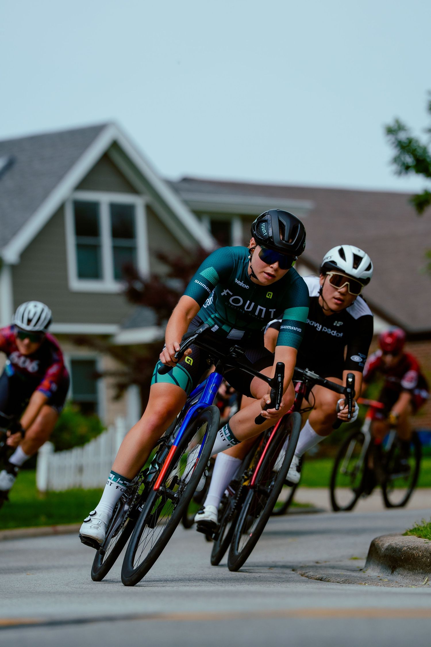 Professional cyclists lean into a sharp turn during a neighborhood road race competition.