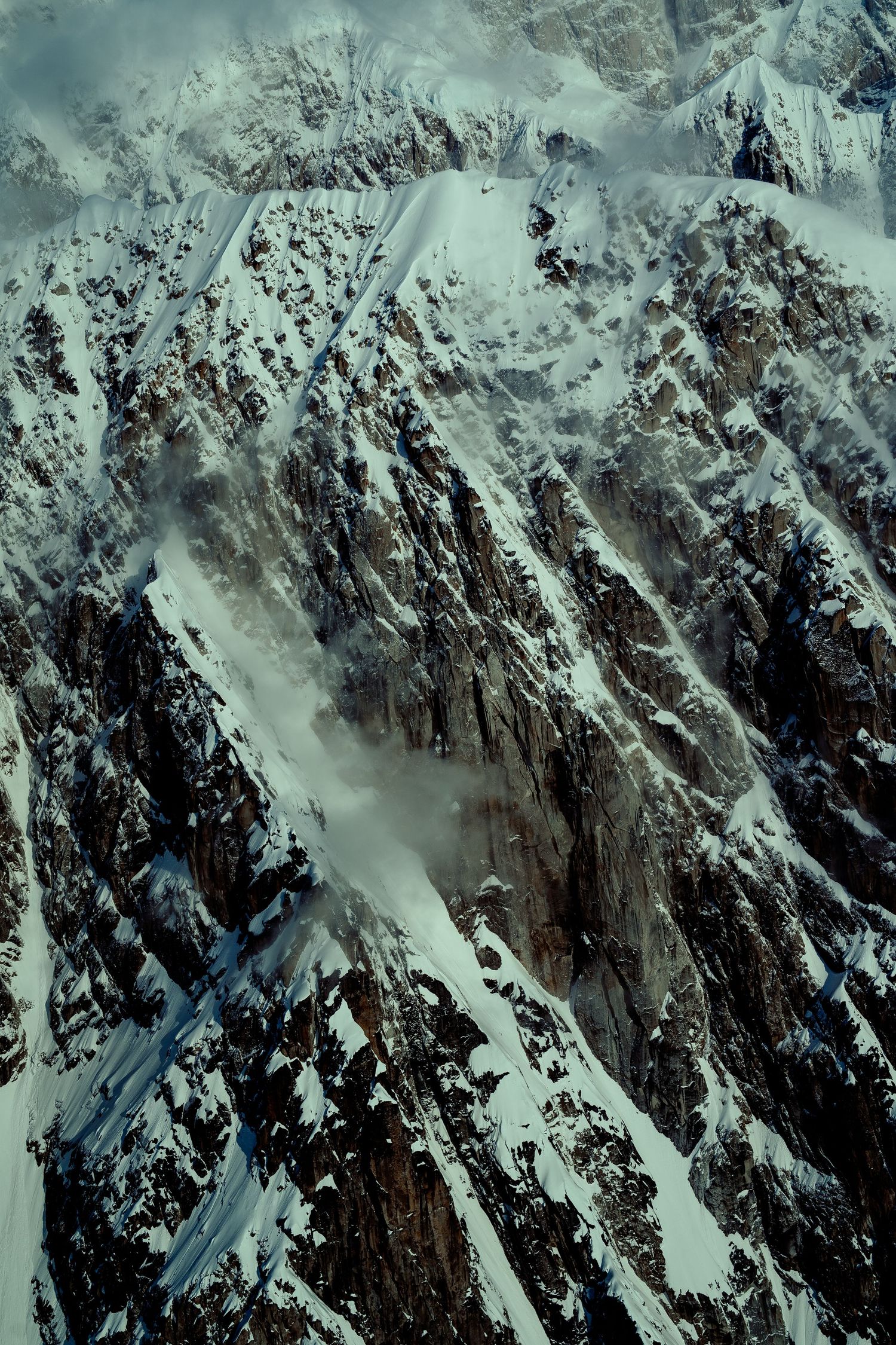 Aerial view of snow-covered jagged mountain peaks with dramatic shadows.
