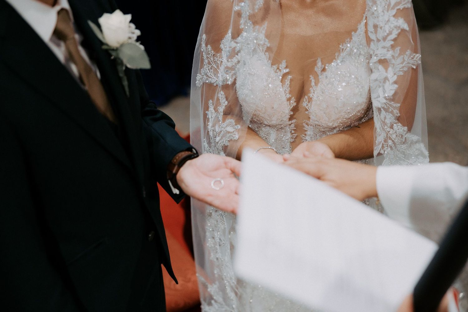 A bride in a white lace wedding dress signs marriage documents with a pen during the ceremony.